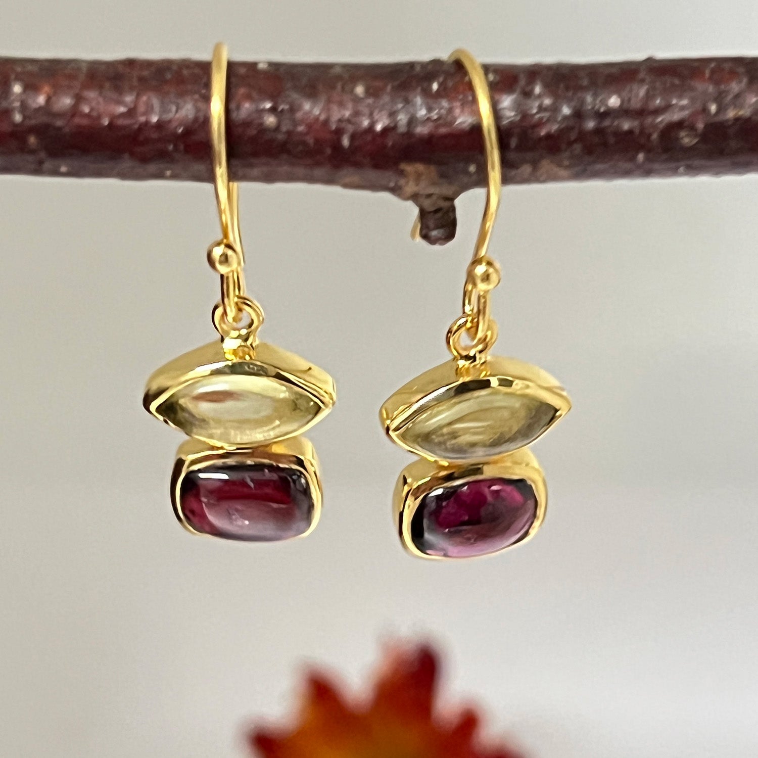 A pair of Fairtrade Beryl Lemon Quartz & Garnet Vermeil Earrings hanging from a twig