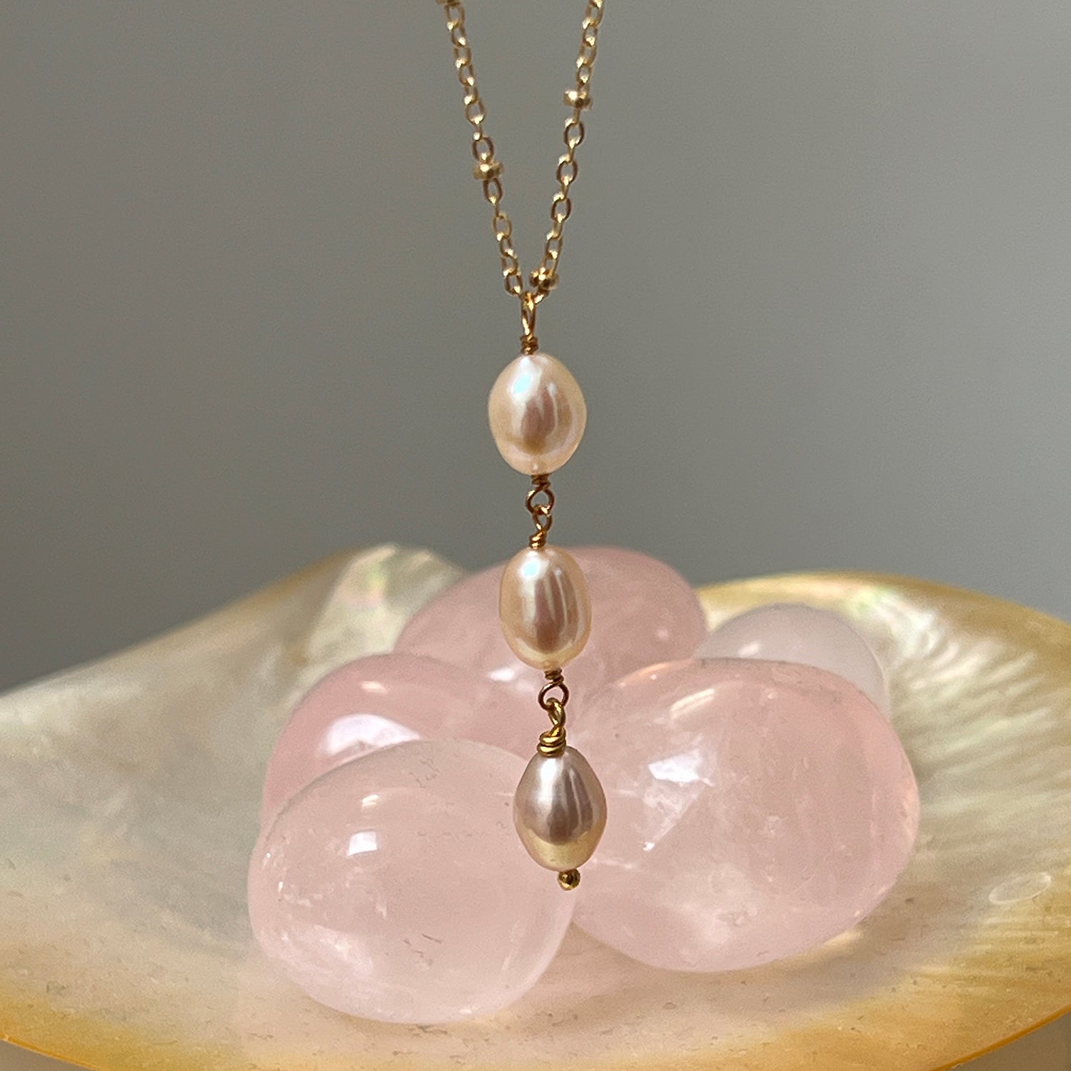 Close-up of a three pink pearl gold-plated satellite chain against a background of pink crystals.