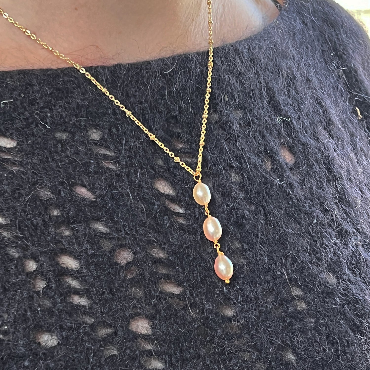 A model wearing a three pink pearl gold necklace on a black sweater.