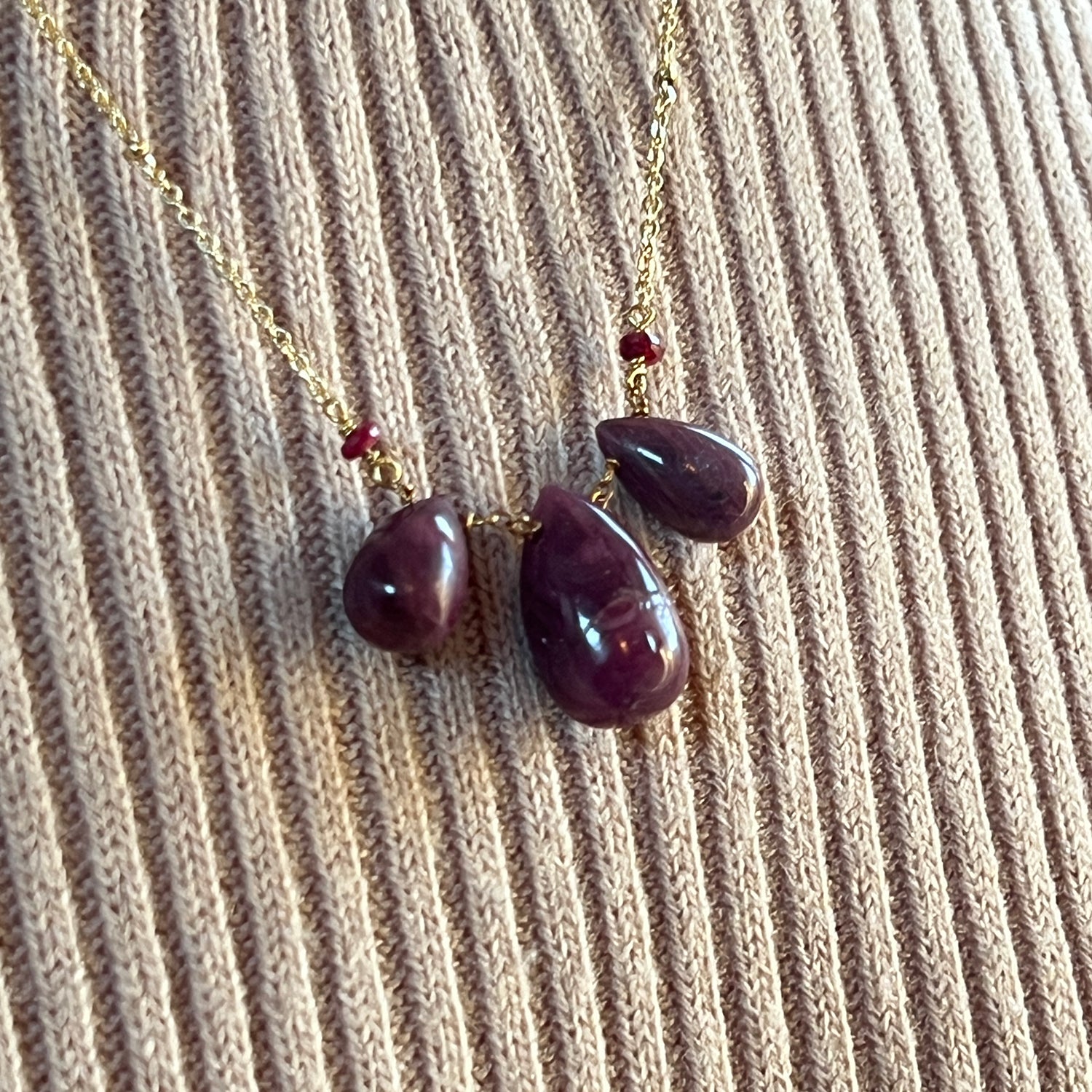 Necklace with teardrop-shaped rubies on a beige jumper