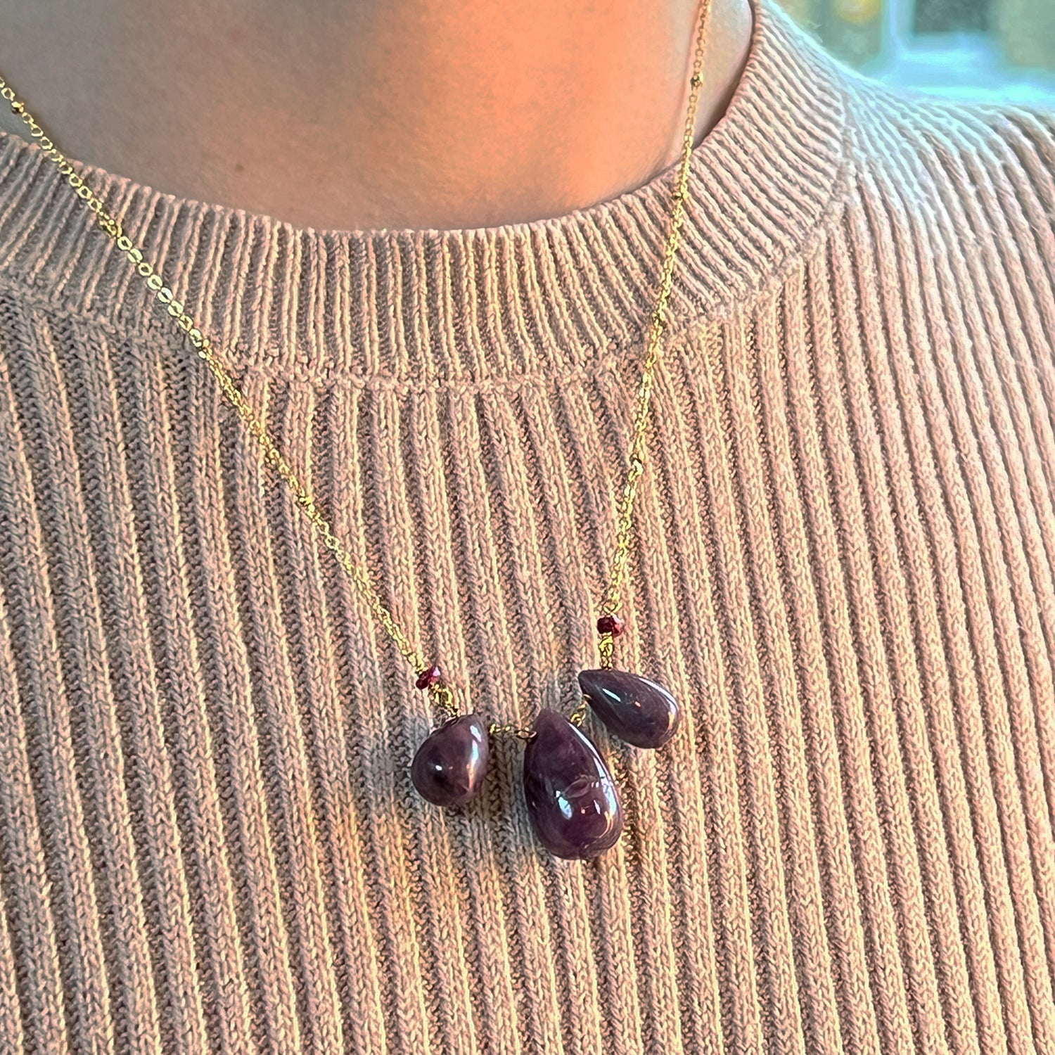 Necklace with three ruby teardrop pendants on a person wearing a beige sweater.