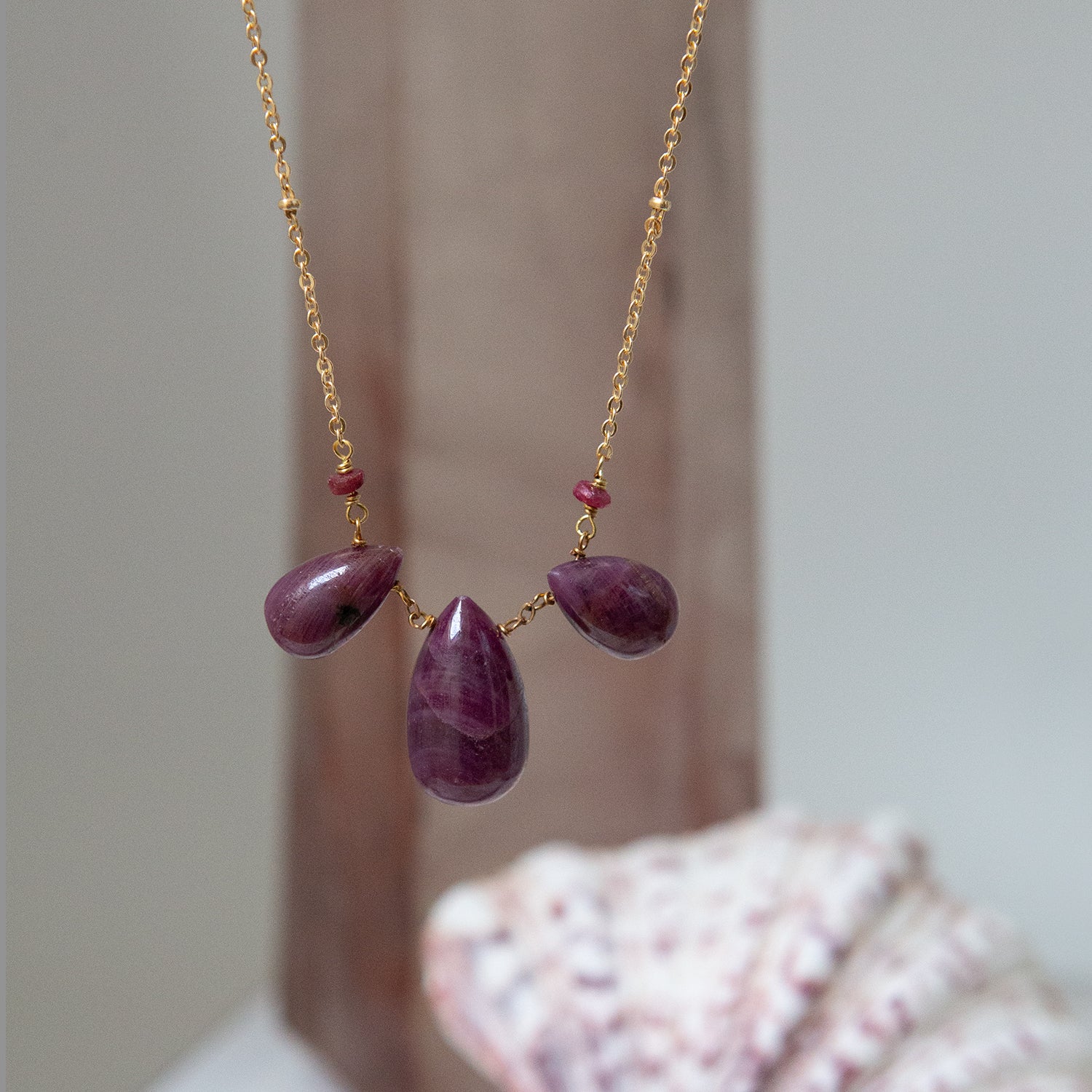Necklace with teardrop-shaped rubies and gold chain on a neutral background
