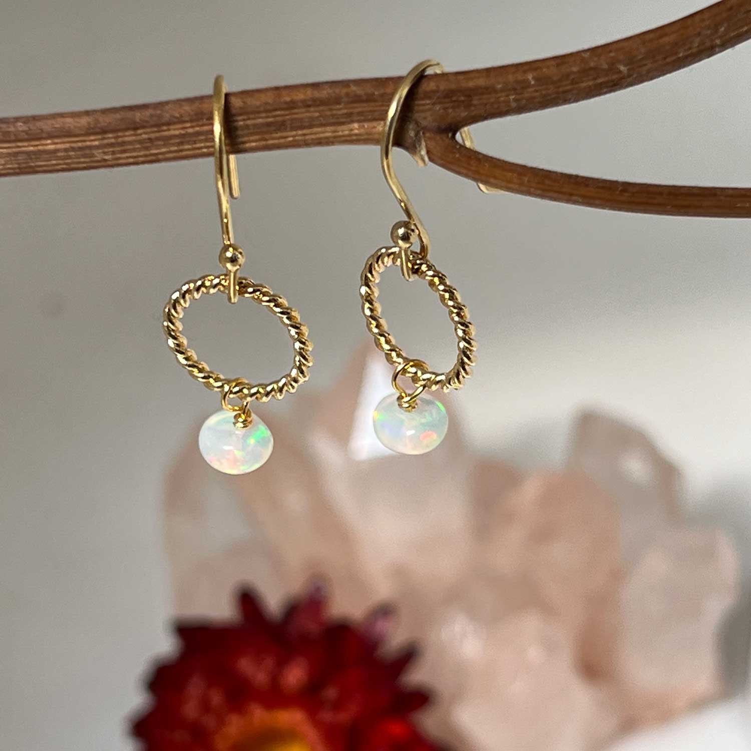 Gold opal loop earrings hanging from a branch