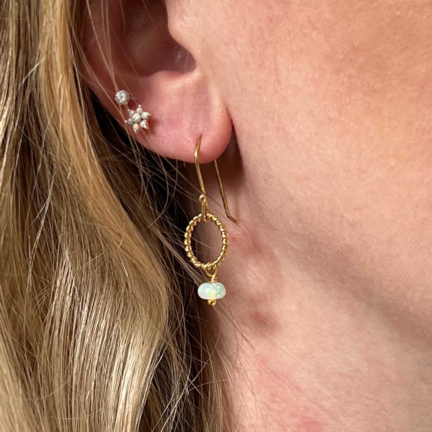 Gold opal loop earring worn on a model.