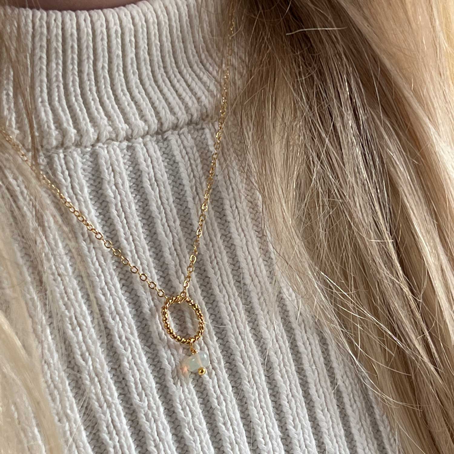 Gold-plated opal pendant necklace worn on a person wearing a cream jumper