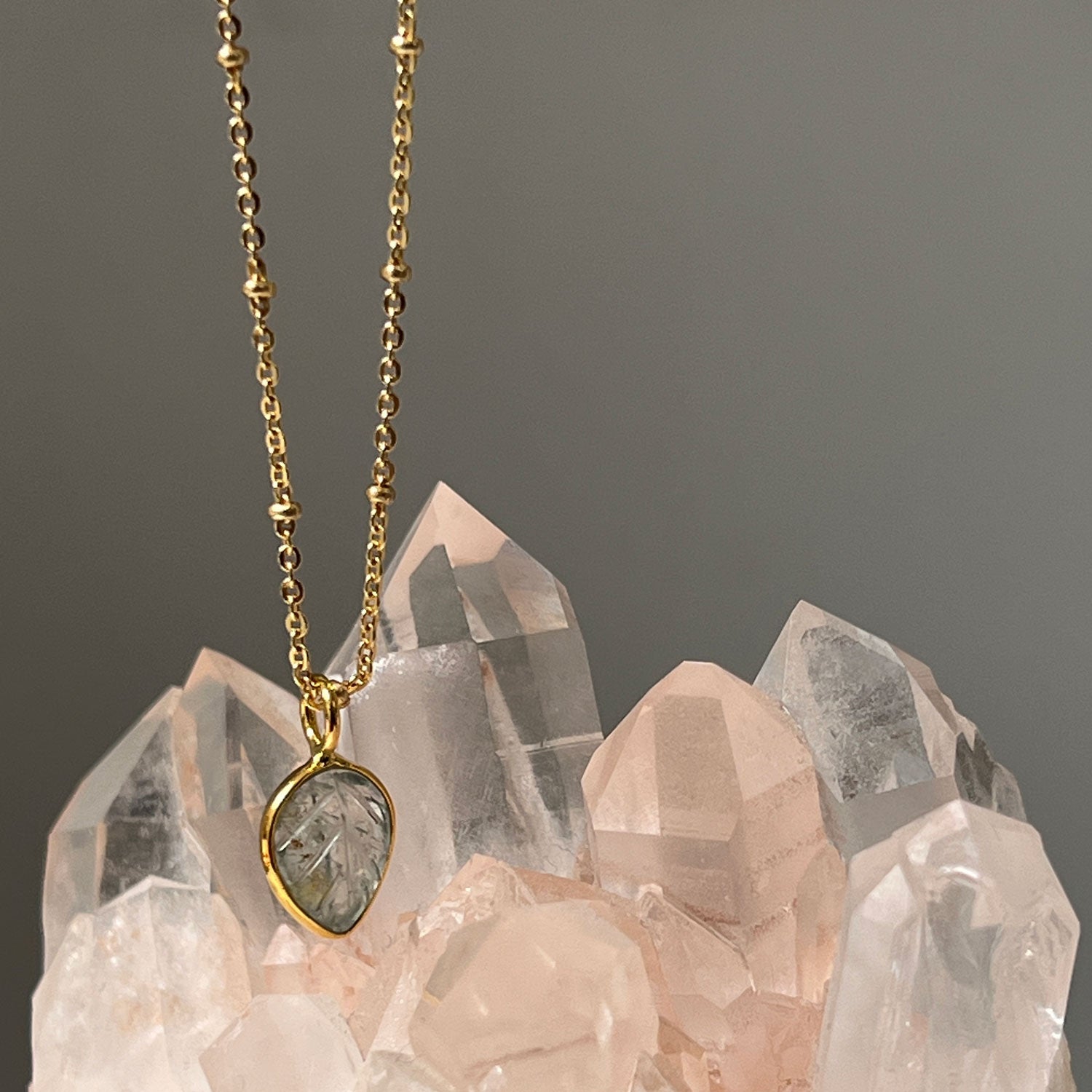 An aquamarine leaf pendant with a gold chain on a background or a crystal