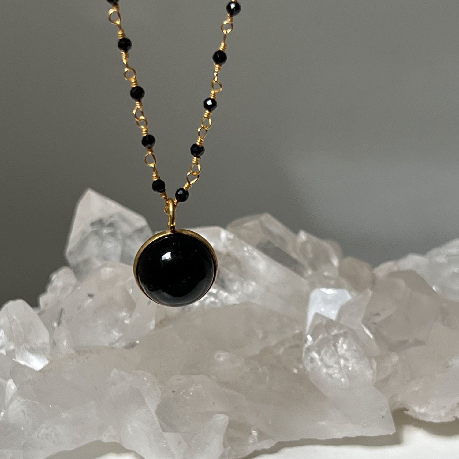 black onyx rosary necklace with a black onyx pendant with a crystal in the background