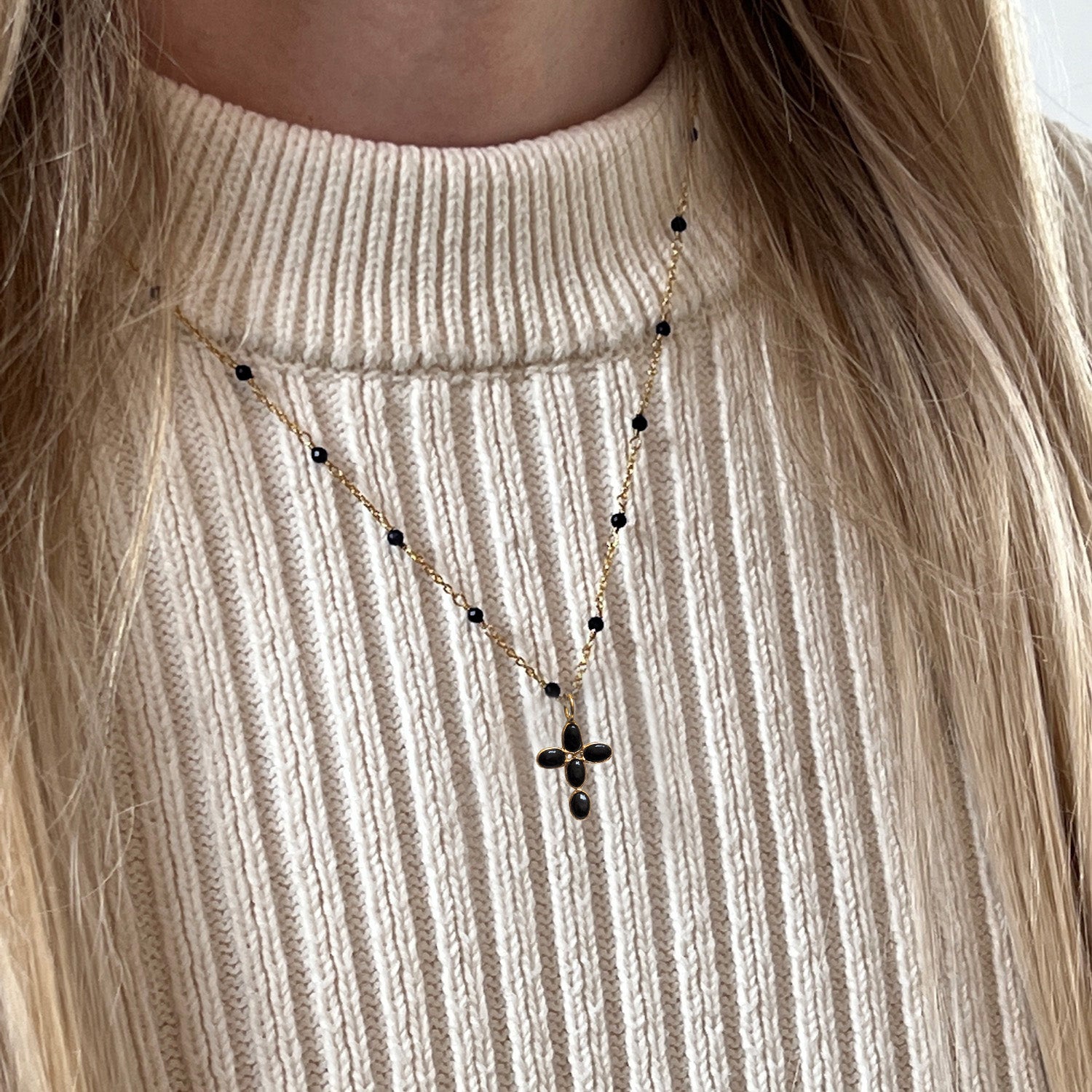 Gold-plated rosary chain with a black onyx cross worn by someone with a cream jumper.