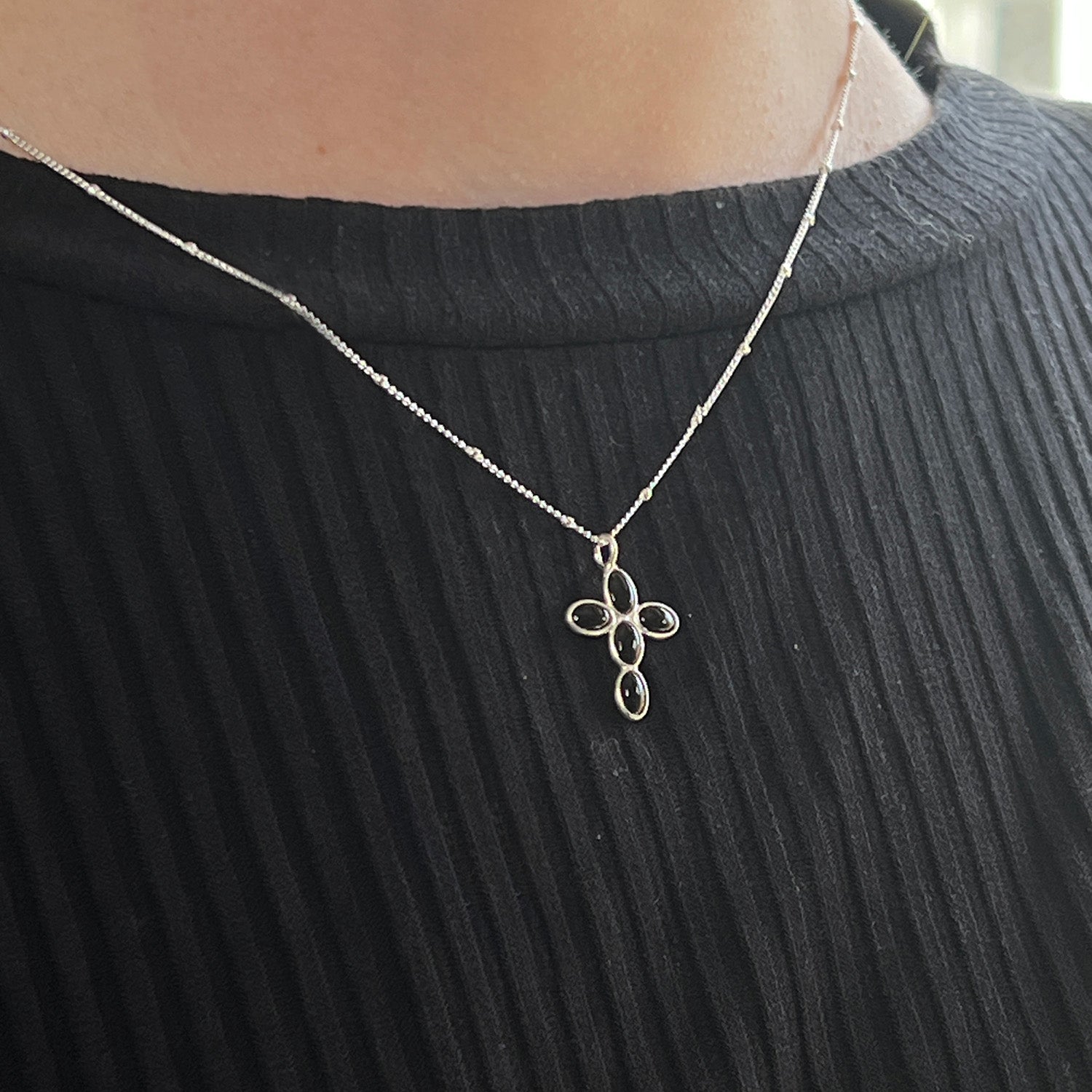Silver necklace with a black onyx cross pendant on a black ribbed sweater