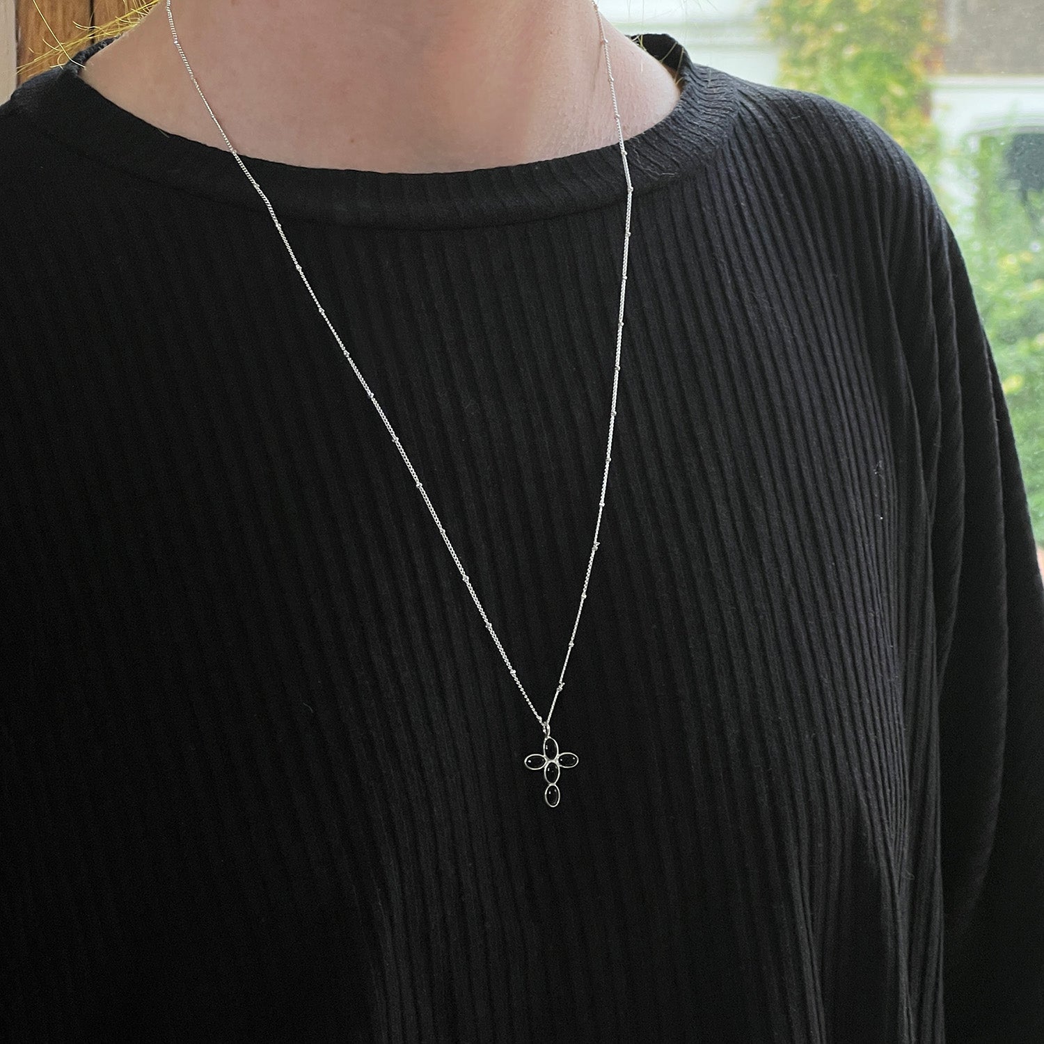 Person wearing a black sweater with a silver necklace featuring a black onyx pendant