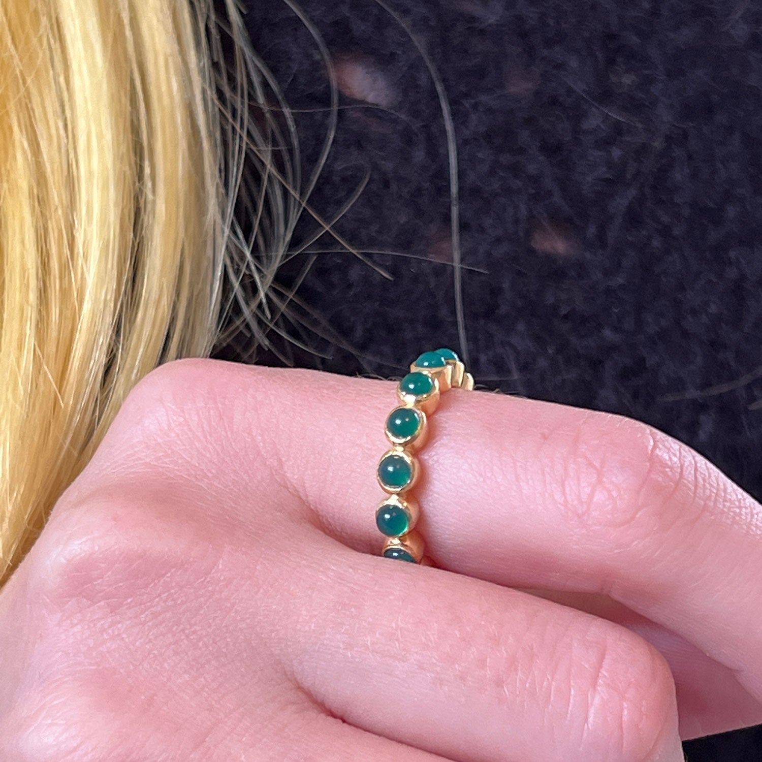 A gold ring with green onyx worn on the hnad of someone wearing a blue sweater.