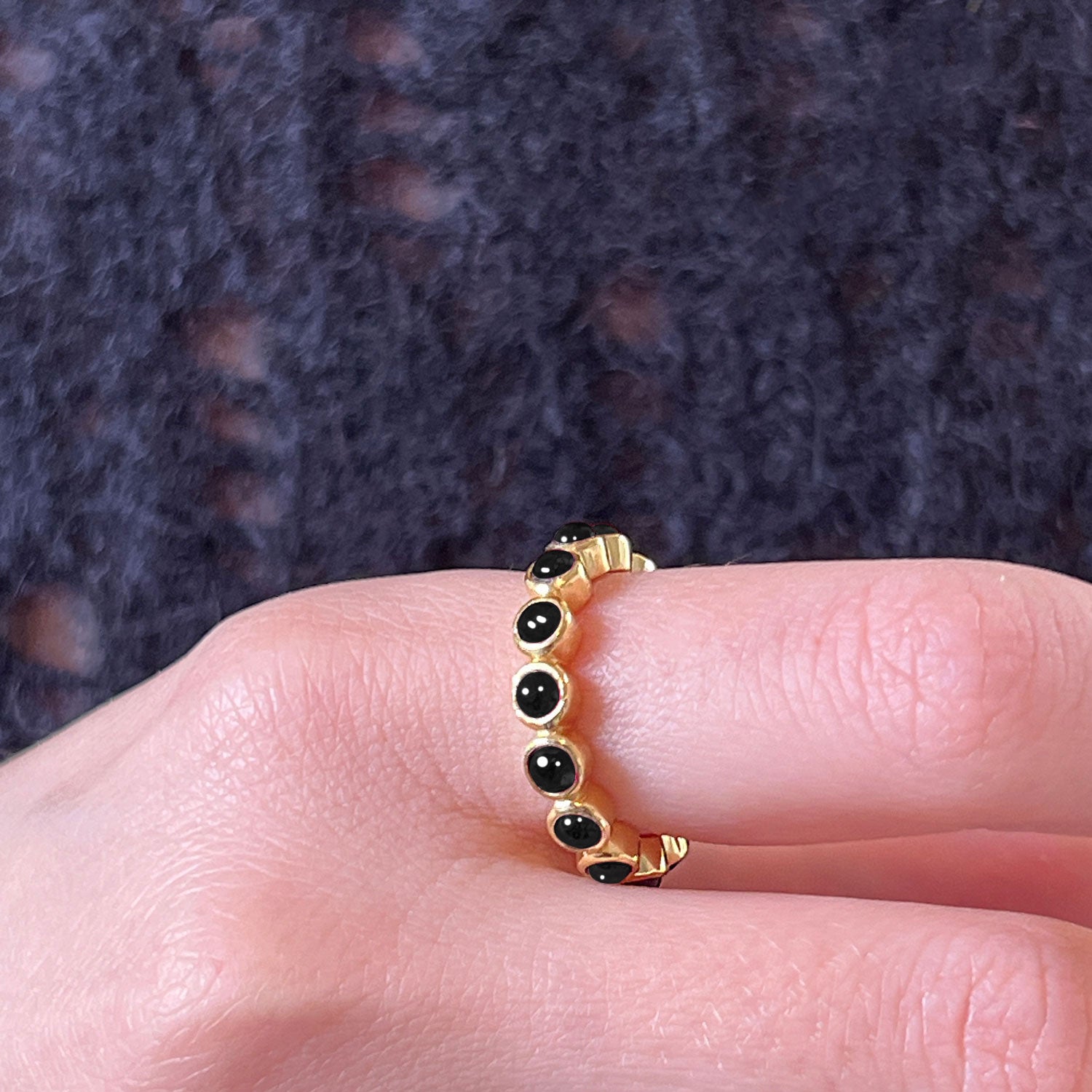 A gold plated black onyx eternity ring worn on a hand against a blue jumper
