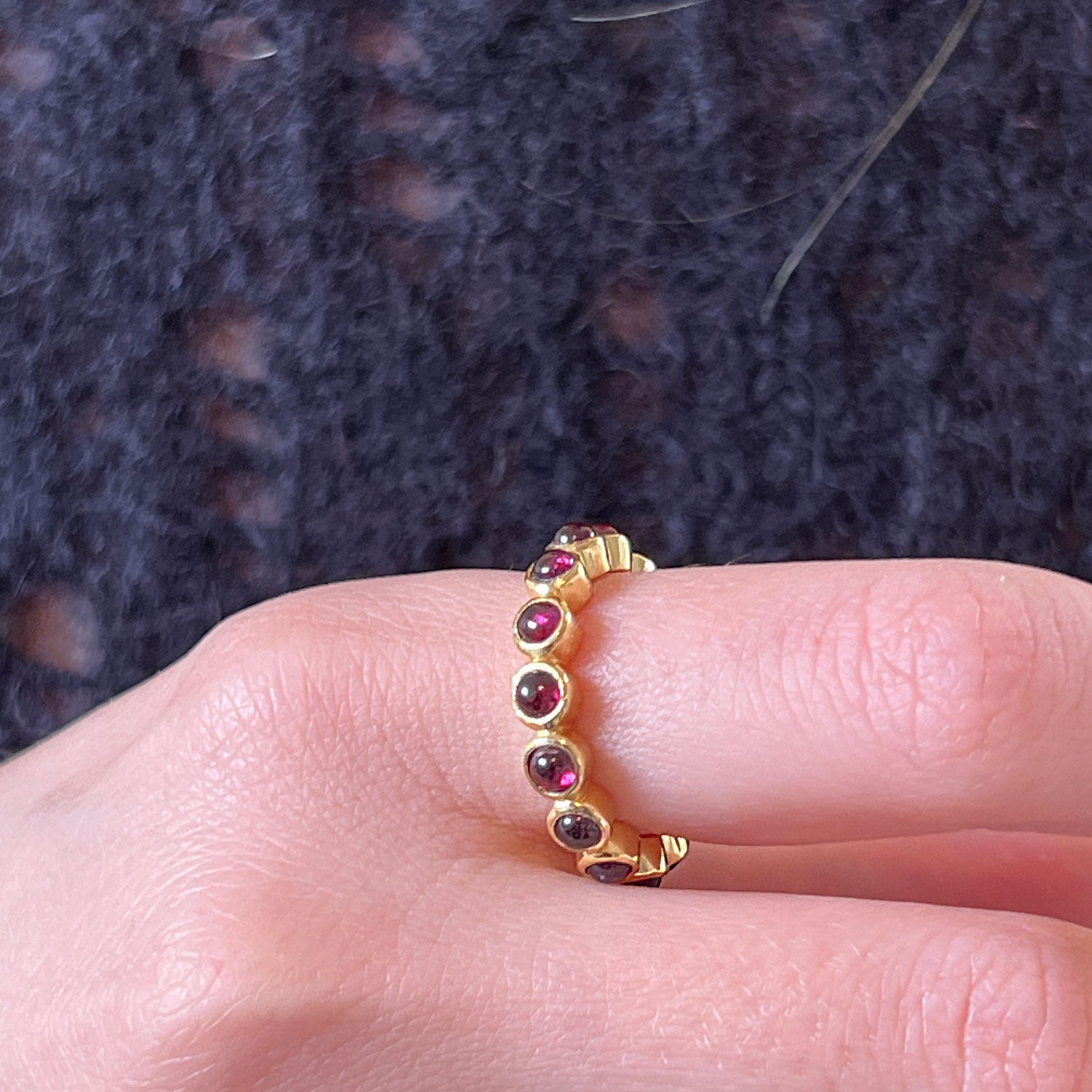 A gold eternity garnet cabochon ring worn on the hnad of someone wearing a blue jumper.