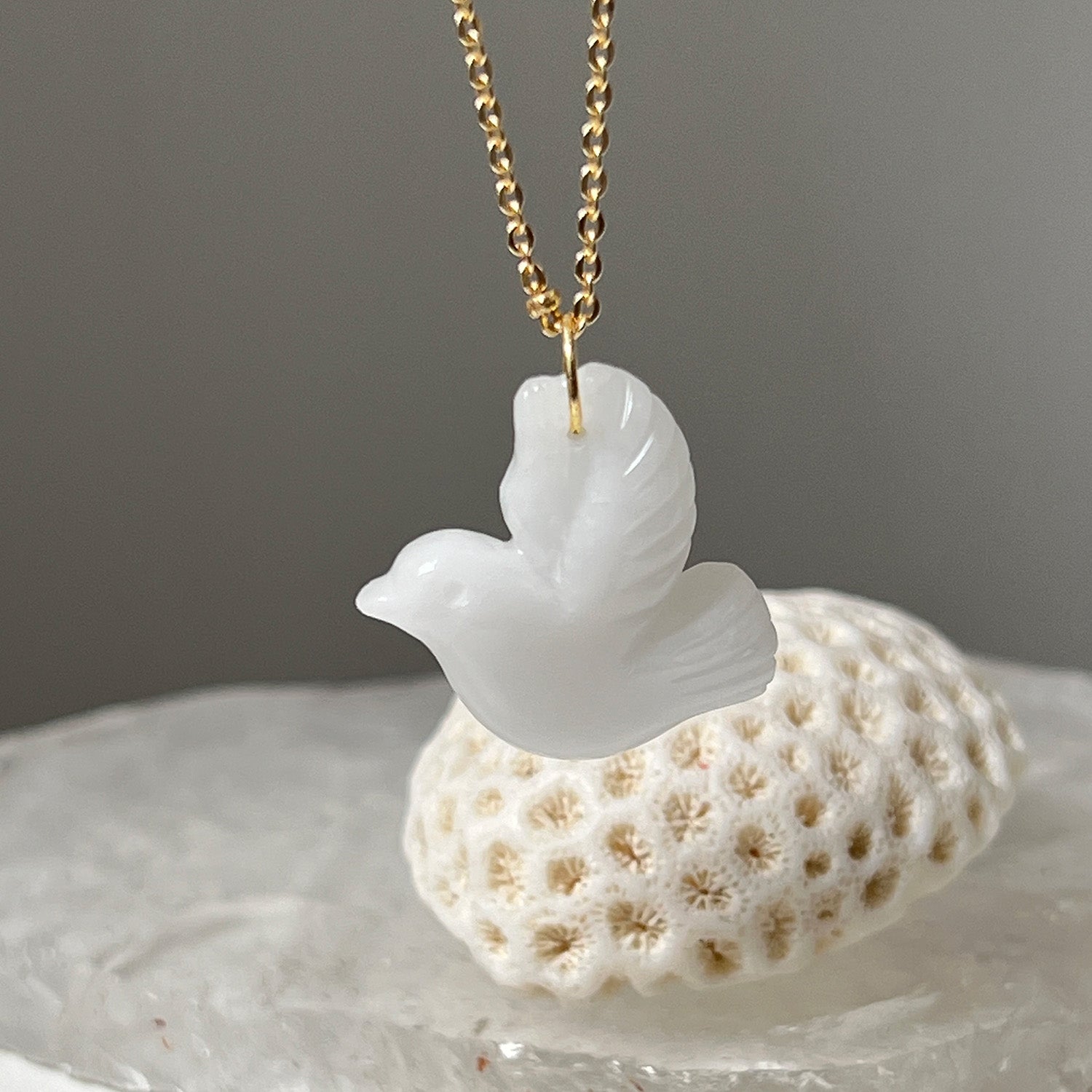A white agate carved in the shape of a dove, attached to a gold-plated long satellite chain, displayed against a neutral background.