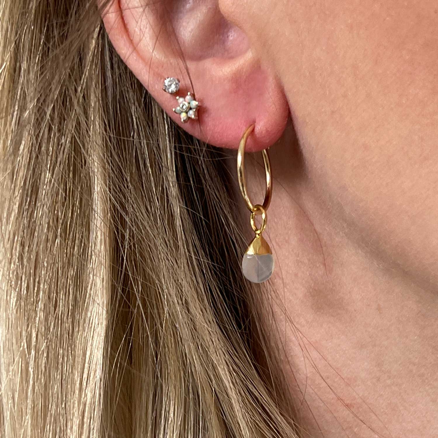 A close-up of a model's ear wearing a gold creol earring with moonstone.