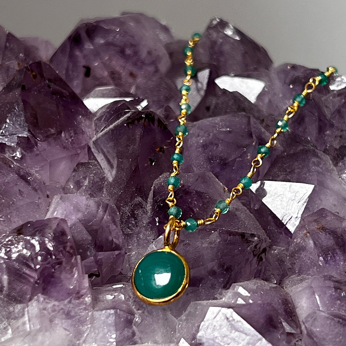 Rosary necklace with a green onyx pendant on a background of purple crystals