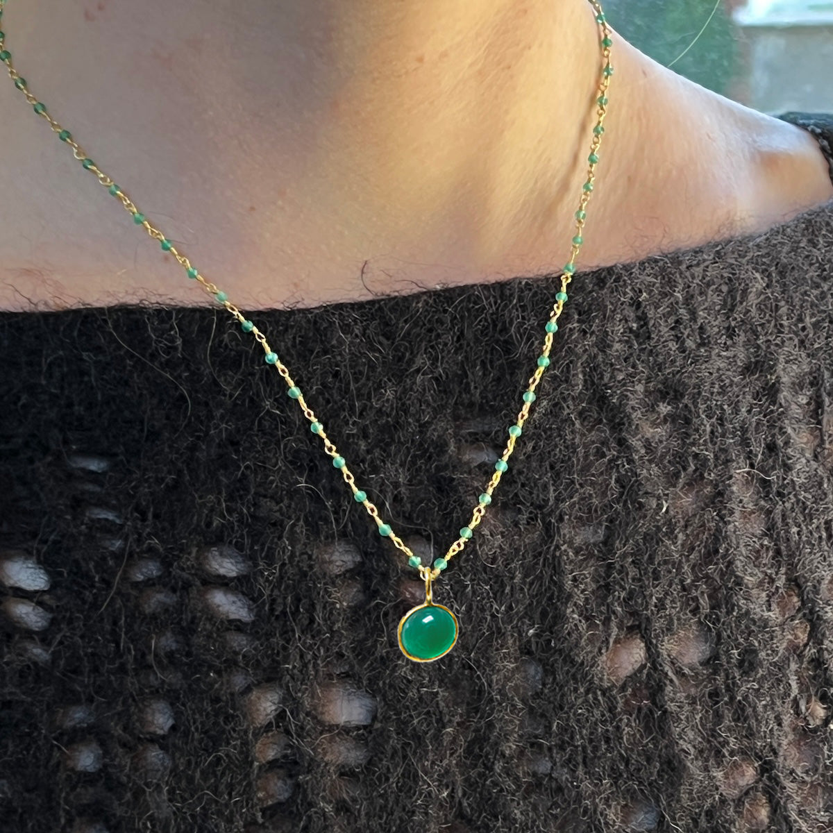 Necklace with a green onyx pendant worn by a person against a dark textured fabric background