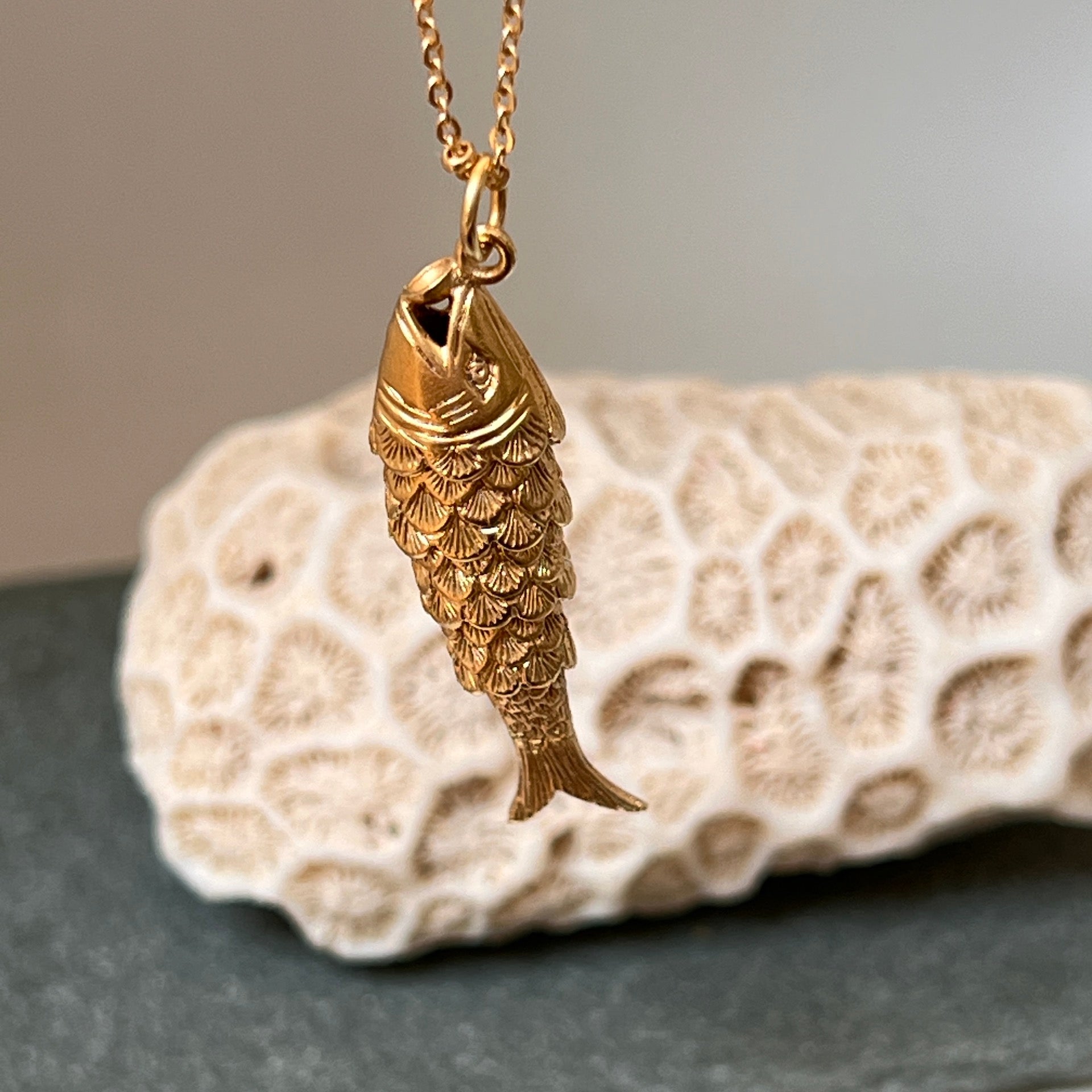 A gold-plated articulated fish charm on a gold satellite chain