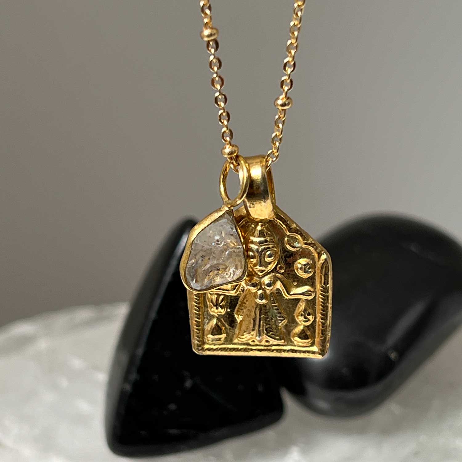 A close up of a gold-plated pendant featuring Goddess Lakshmi with a Herkimer Diamond