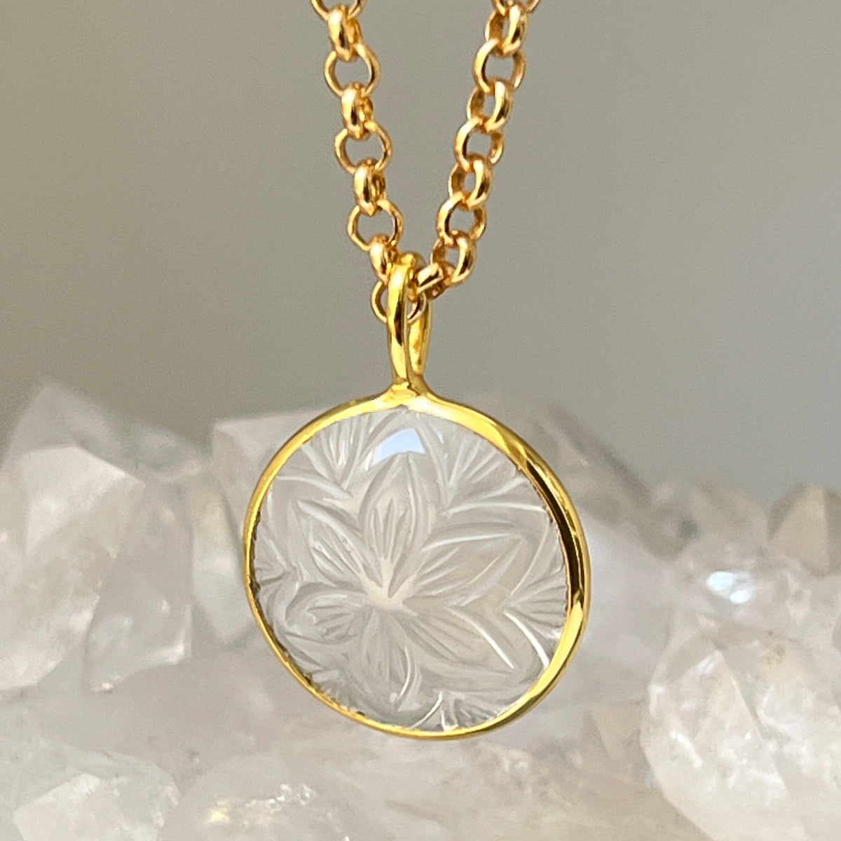 Gold necklace with a clear pendant featuring floral engraving on a textured surface.