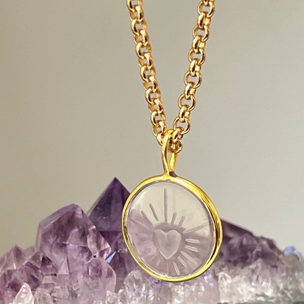 Gold necklace with a heart pendant on a background of amethyst crystals