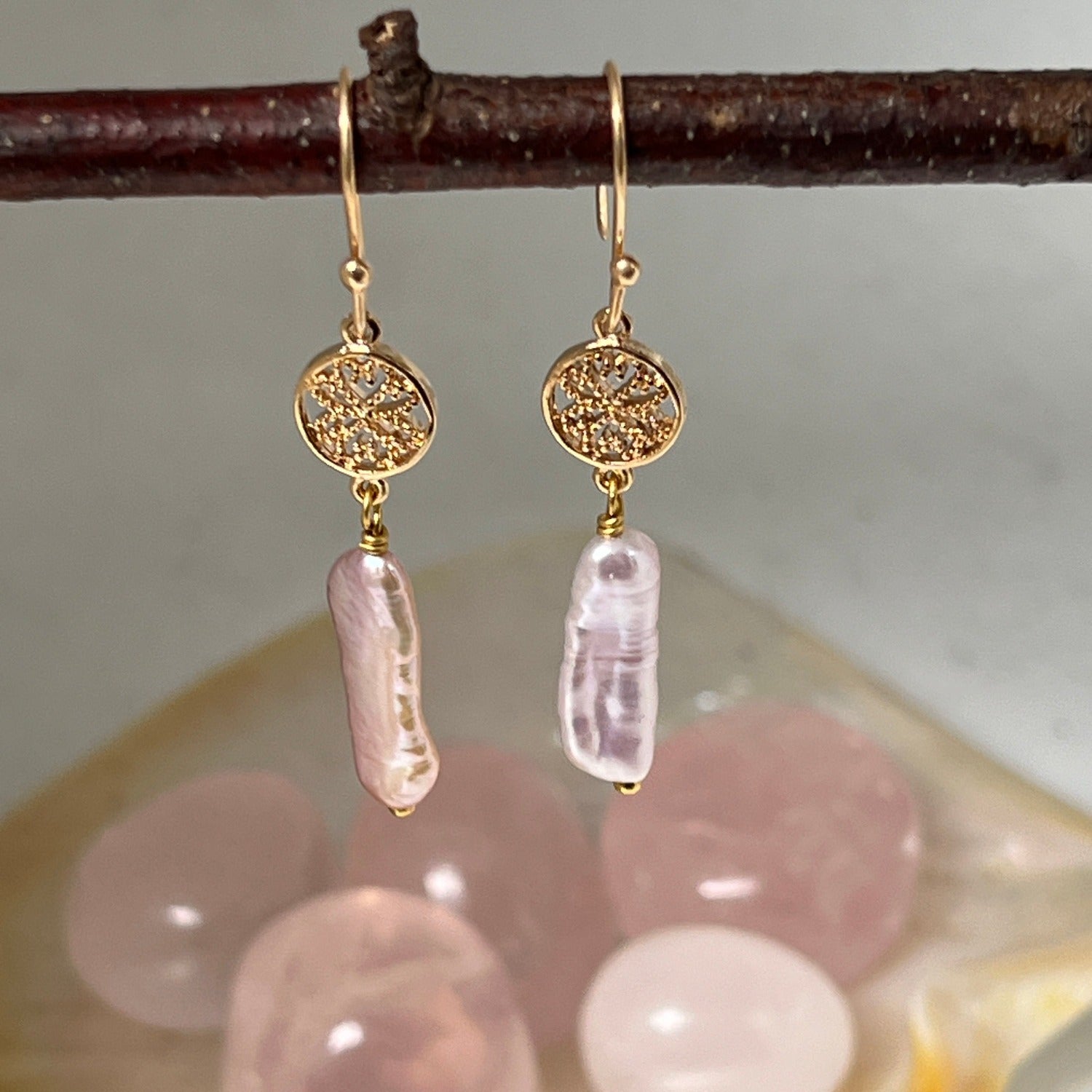 G gold-plated baroque pink pearl earrings, hanging from a twig with crystals in the background