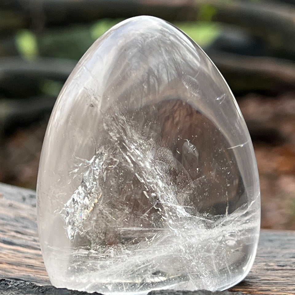 Clear polished crystal rock on a wooden surface with a blurred natural background