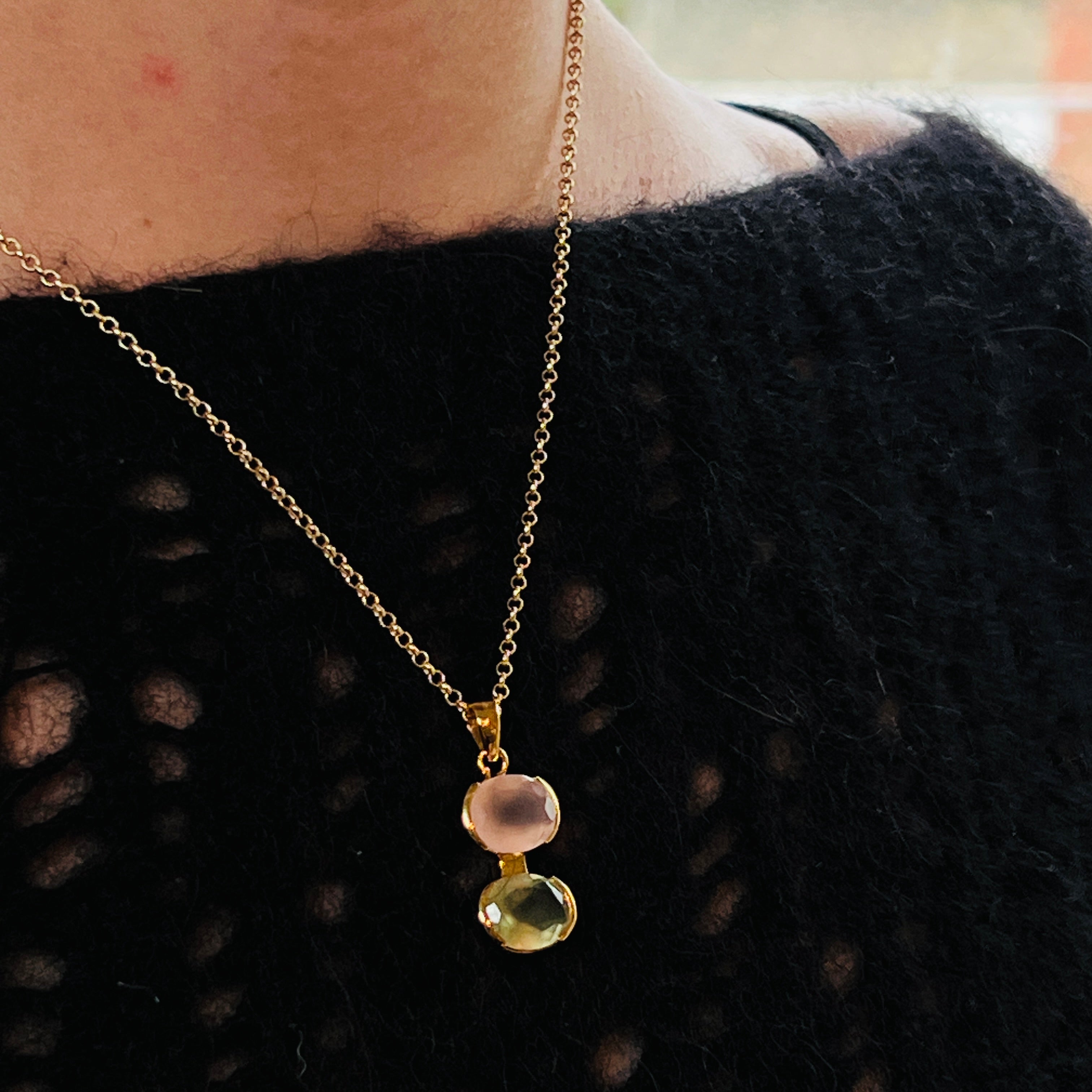 Close up of a gold necklace with a rose quartz and prehnite pendant worn by a person wearing a black jumper