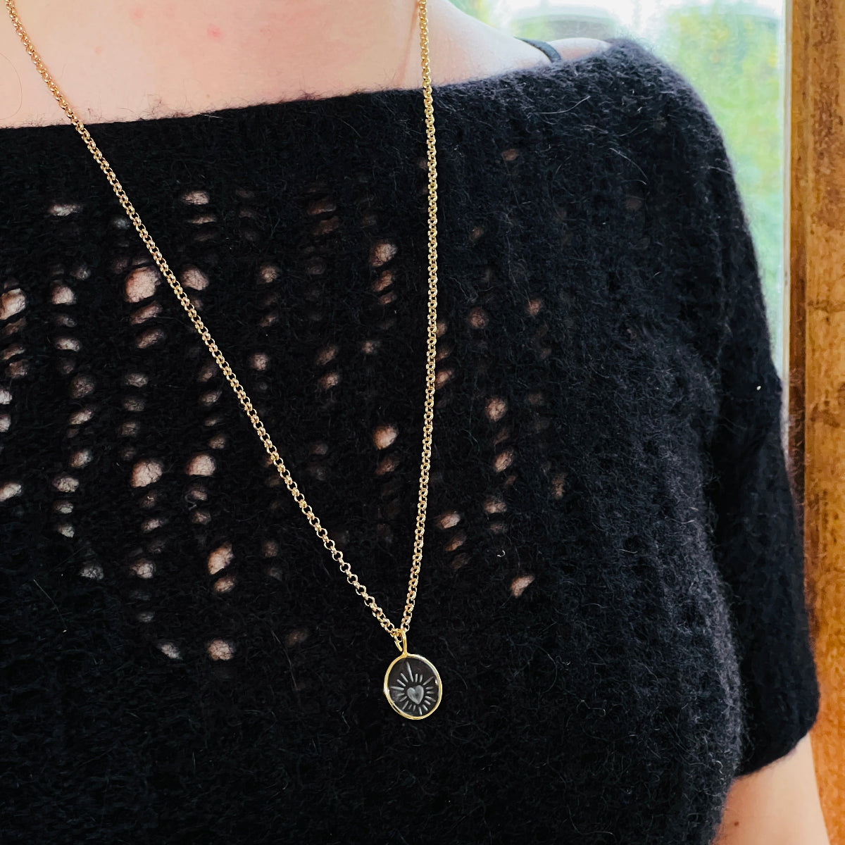 Gold necklace with a hand-carved pendant on a person wearing a black sweater.