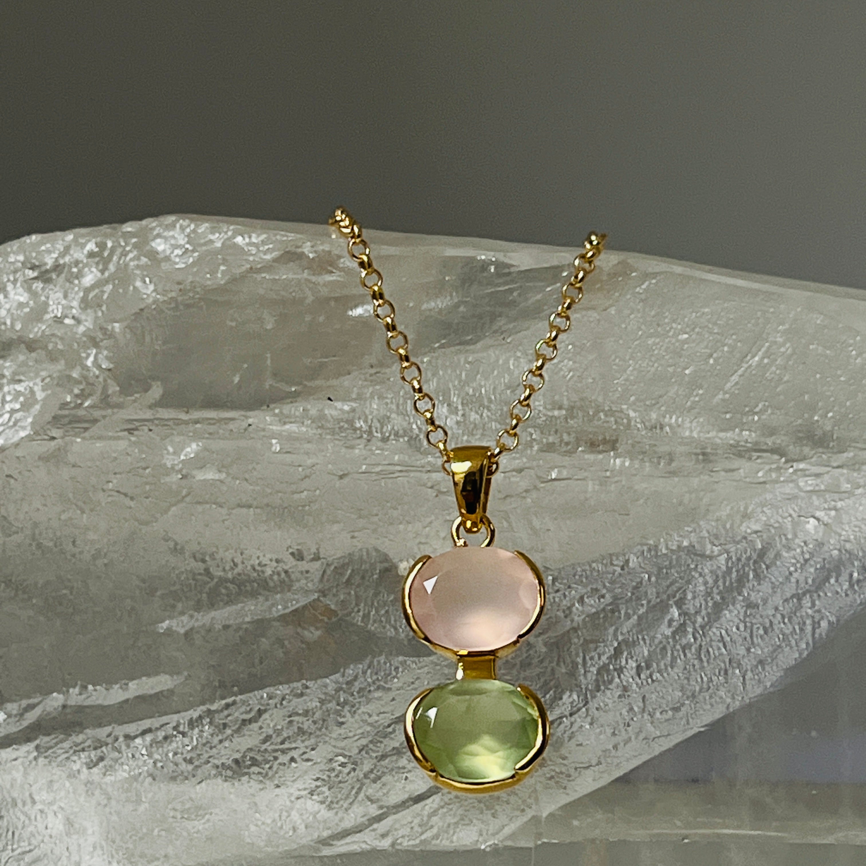 Gold necklace with two gemstones on a stone surface