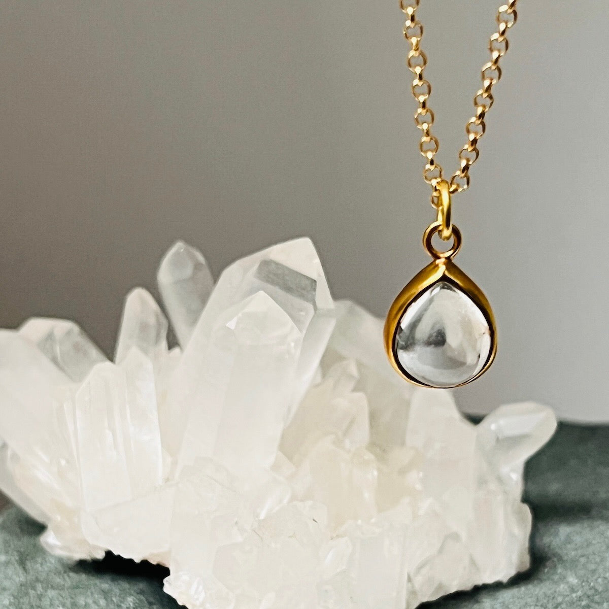Gold necklace with a teardrop rock crystal pendant on a grey background