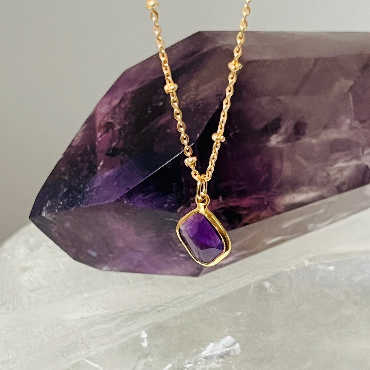 Gold necklace with a purple amethyst pendant on a crystal background