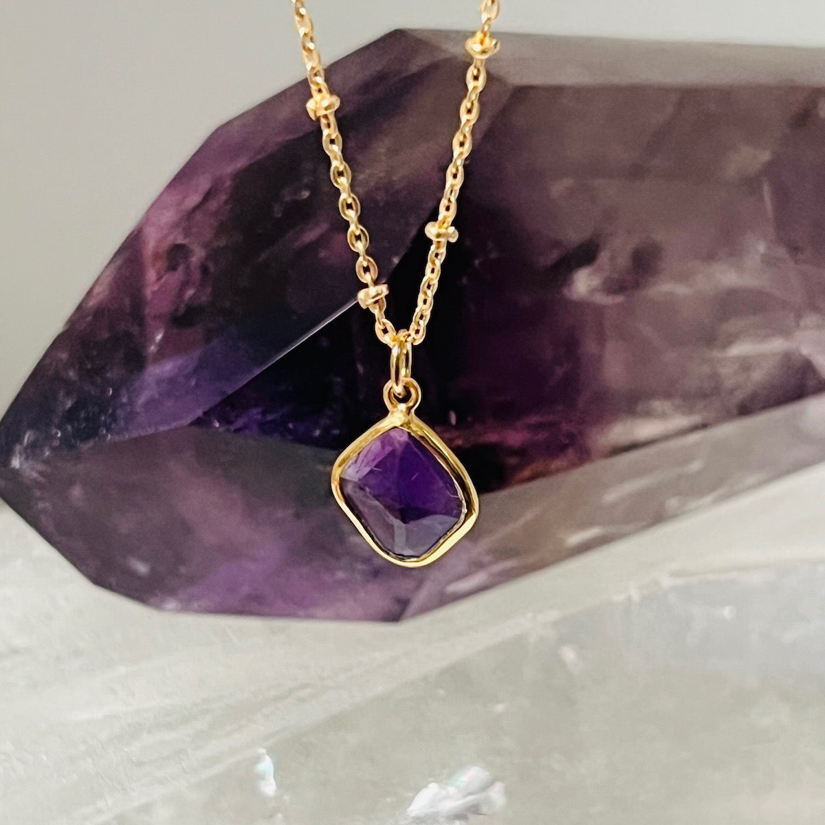 Gold necklace with a purple amethyst pendant on a purple crystal background