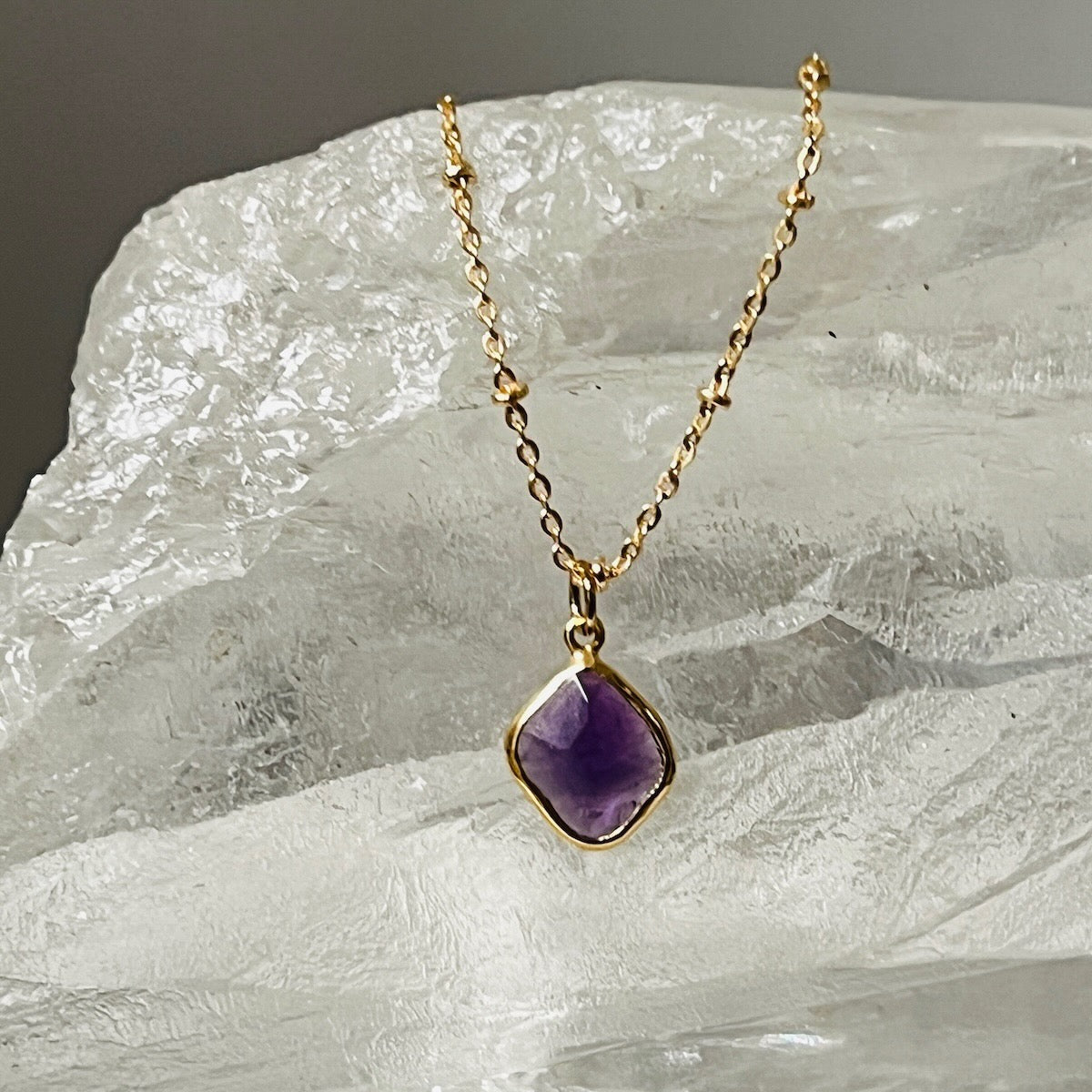 Gold necklace with a purple amethyst pendant on a textured stone surface
