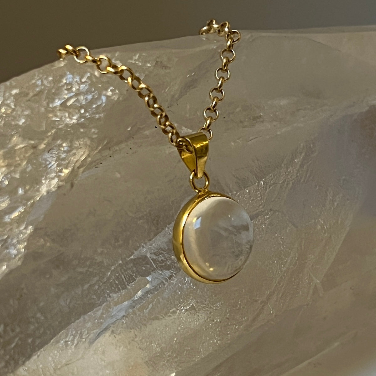Gold necklace with a clear rock crystal pendant on a textured stone surface