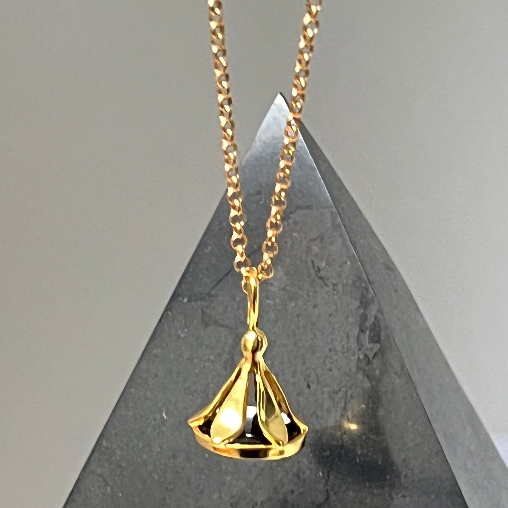 Gold necklace with a stamp pendant on a grey stone pyramid surface