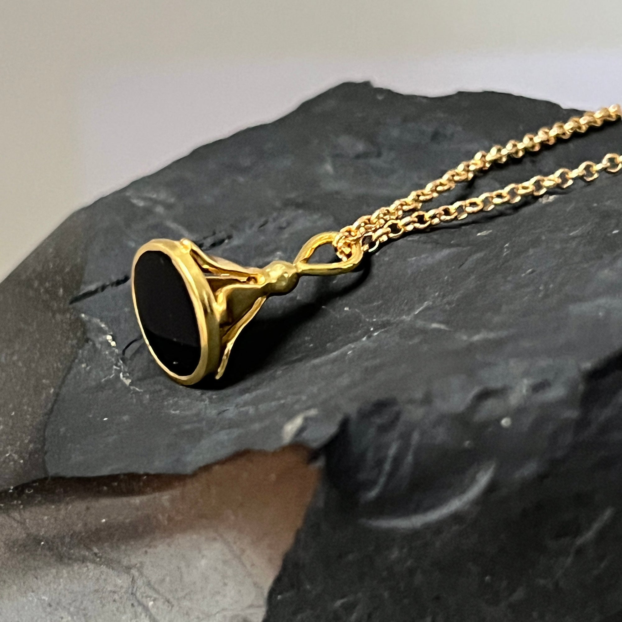 Gold necklace with a black onyx stamp pendant on a dark stone surface