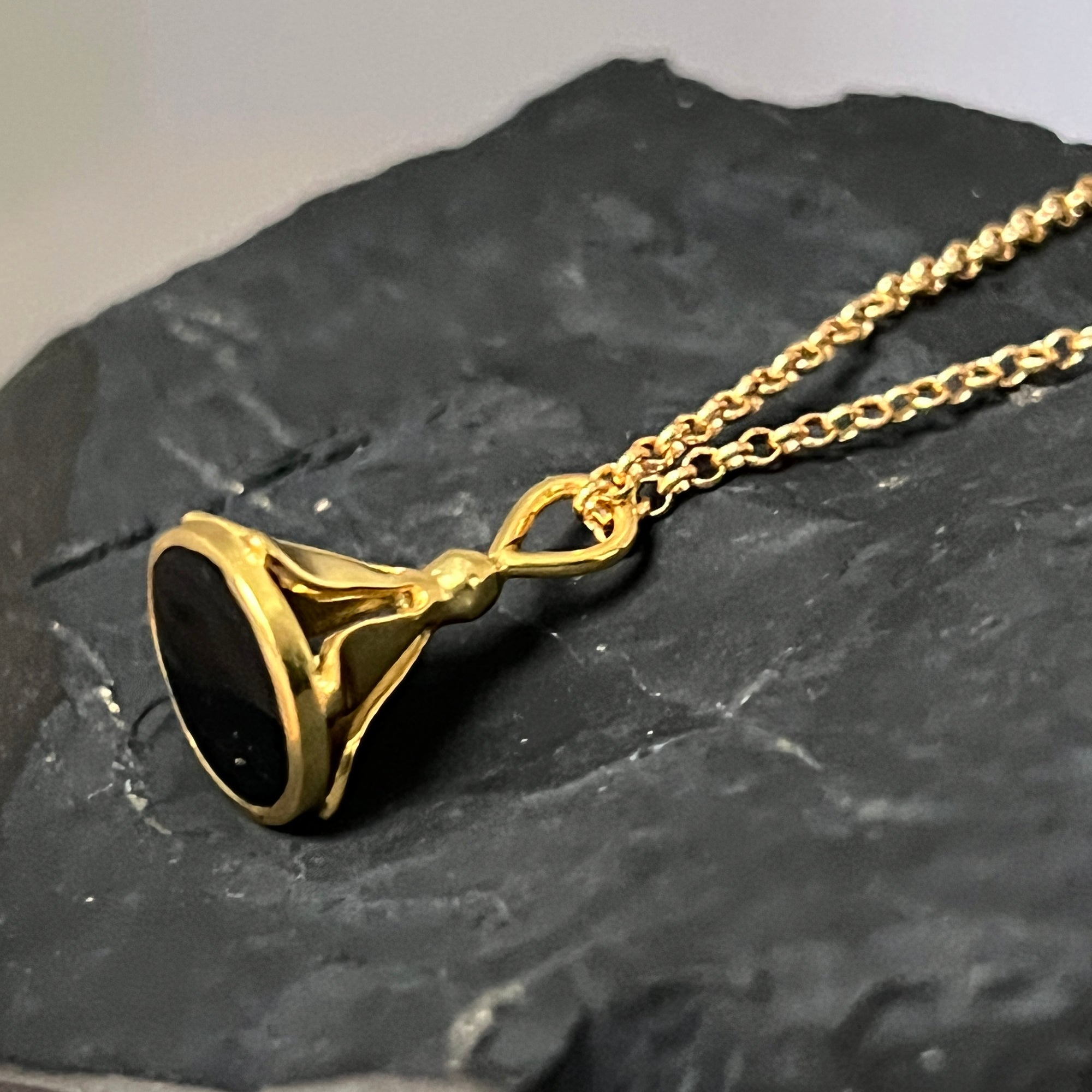 Gold necklace with a black onyx pendant on a dark stone surface
