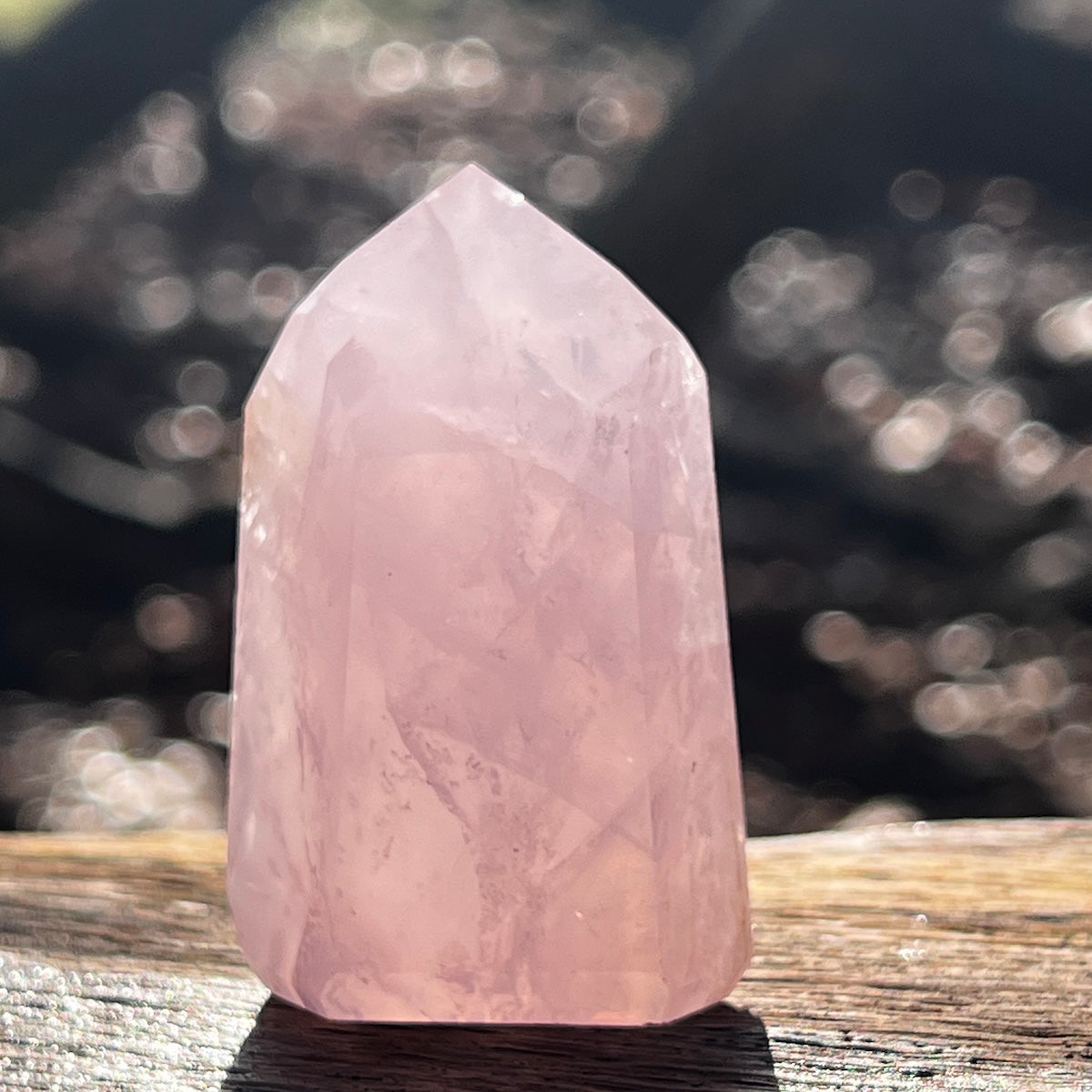 Rose quartz crystal point on a wooden bench with a blurred background