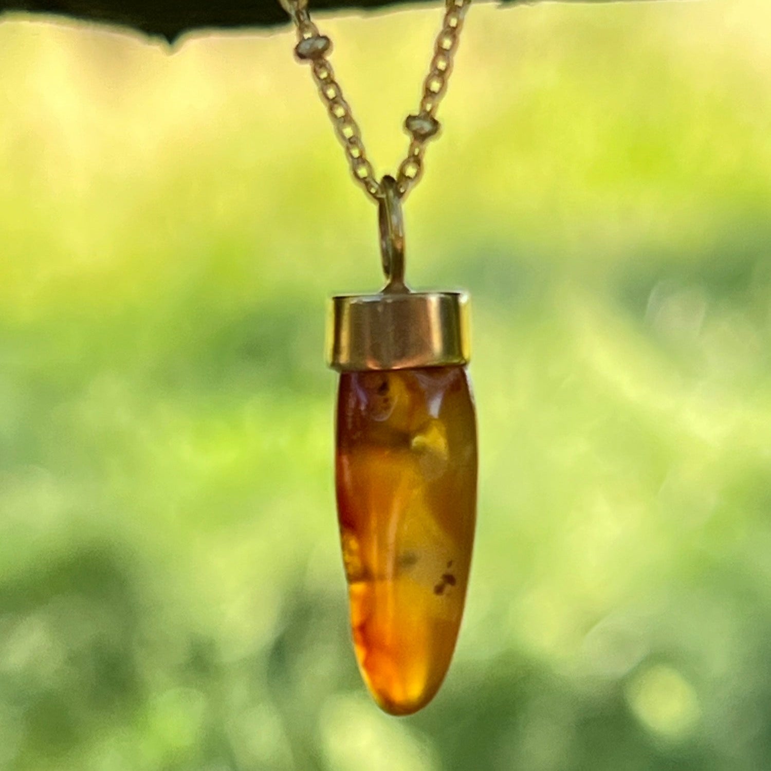 Carnelian pendant necklace with gold chain against a blurred green background