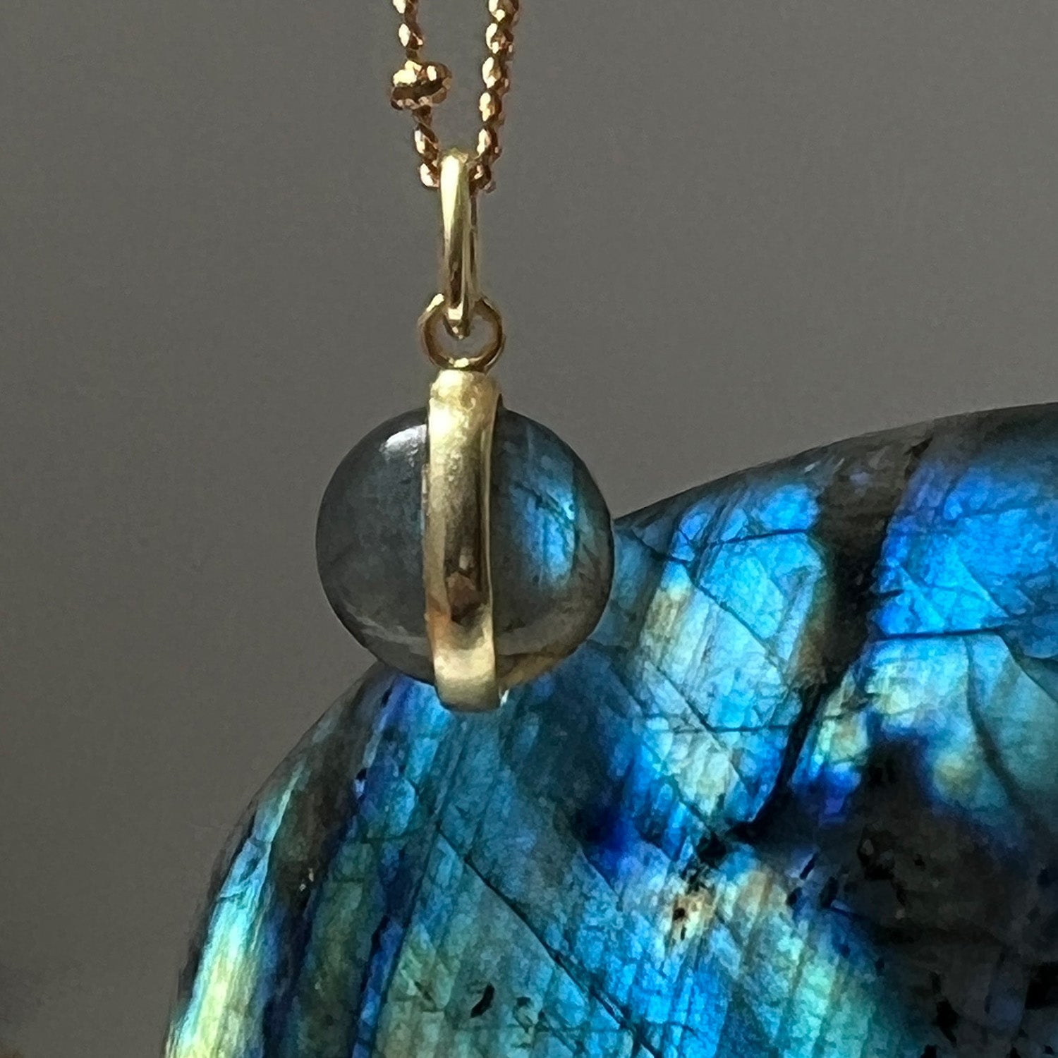 Gold pendant on a chain with a blue Labradorite gemstone against a grey background