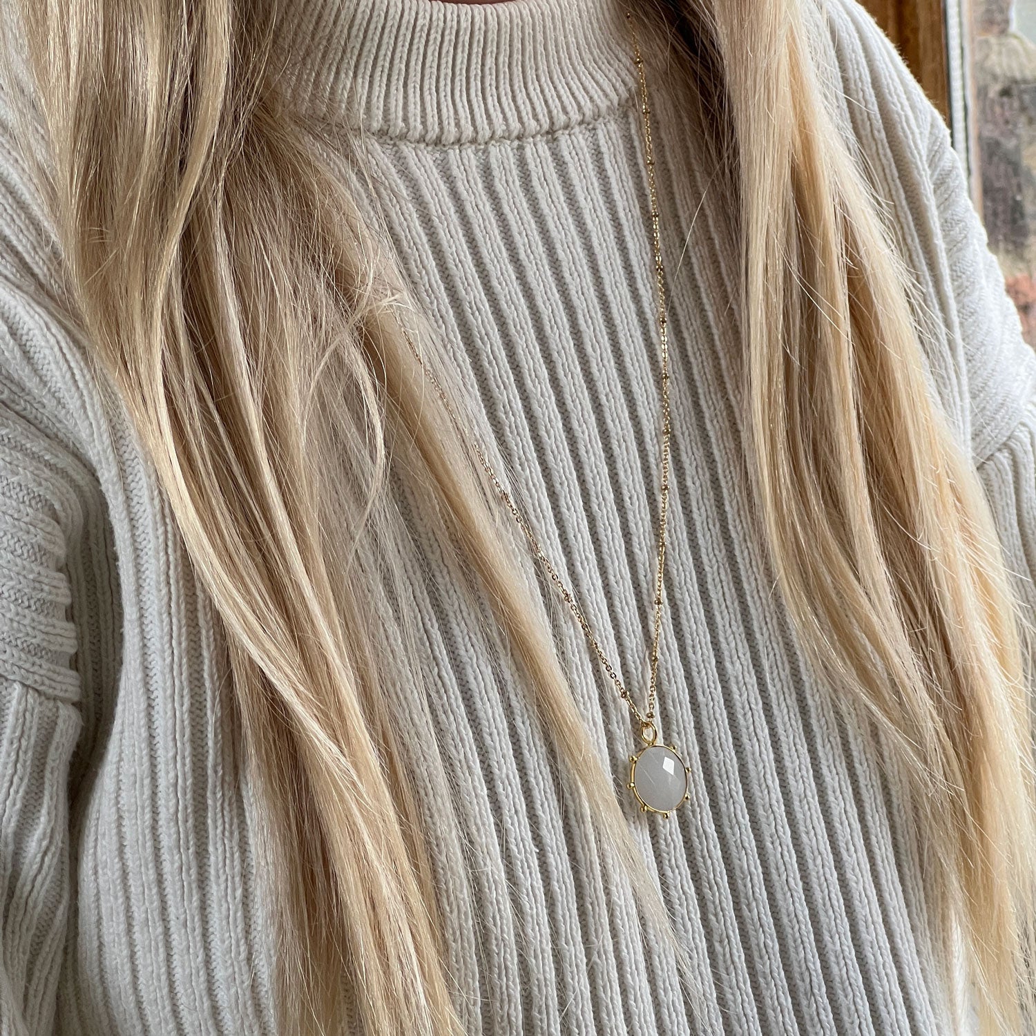 White chalcedony pendant on a long gold necklace, worn by a model with blonde hair and a cream jumper.