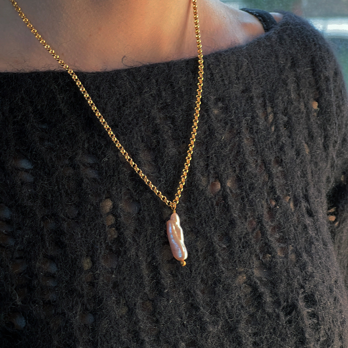 Gold chain necklace with a unique pearlpendant on a dark sweater