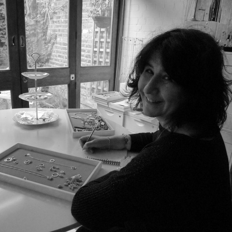 Black and white photo of Veronique working with jewellery at a table.