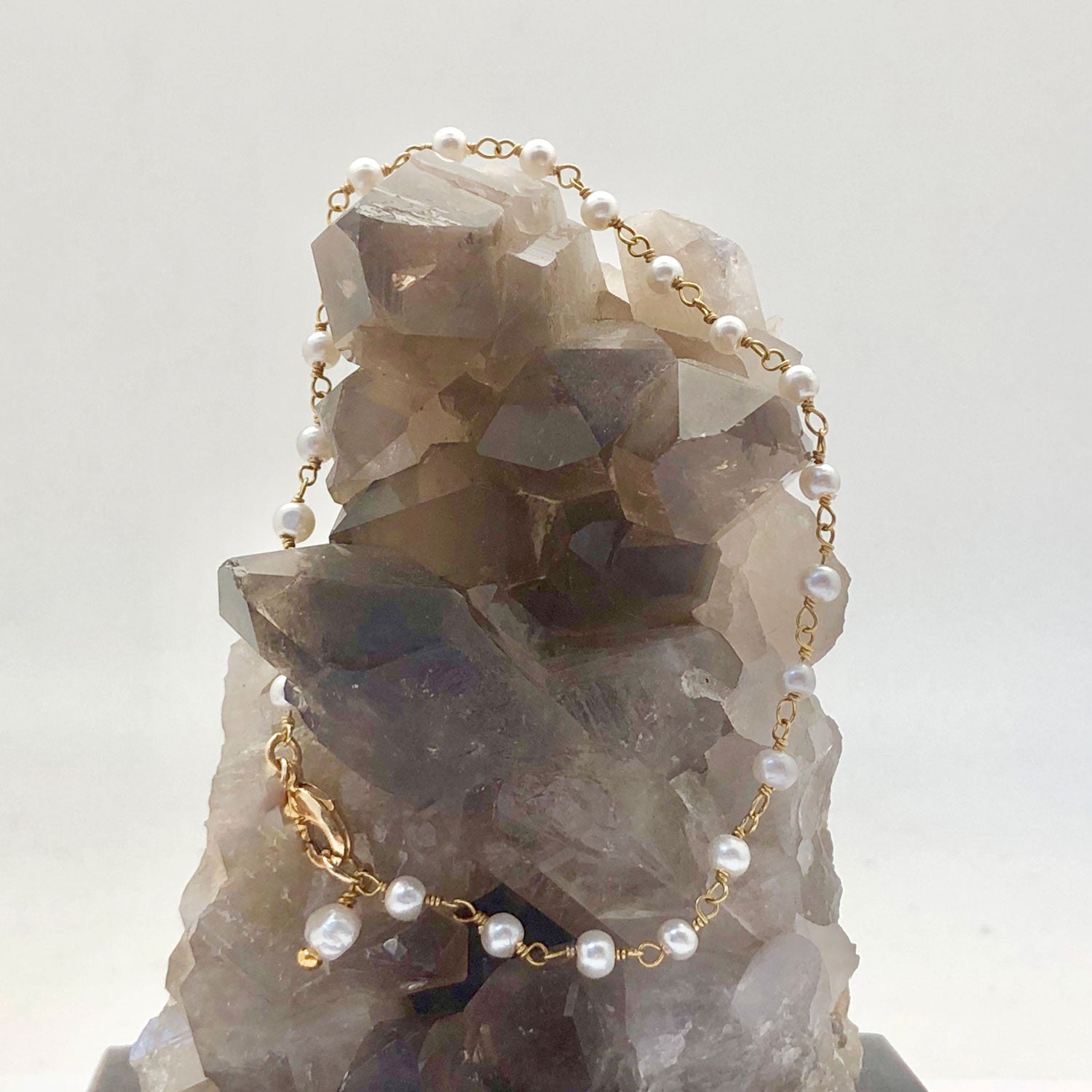 A gold-plated white freshwater pearl roasry bracelt on a grey crystal