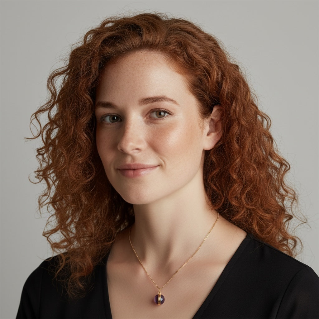 Woman with curly red hair wearing a black top and gold amethyst necklace against a neutral background