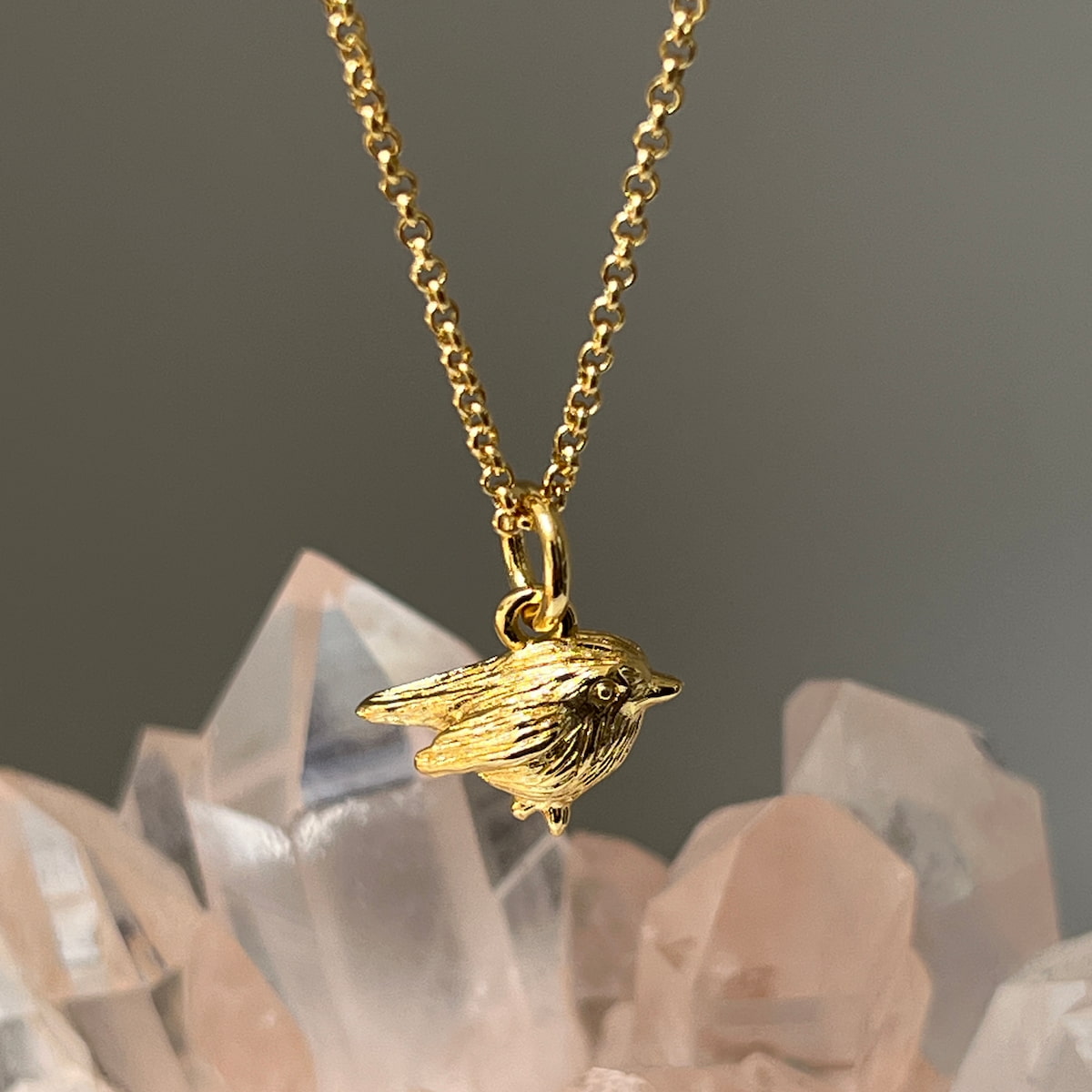 Gold robin pendant necklace on a chain with crystals in the background
