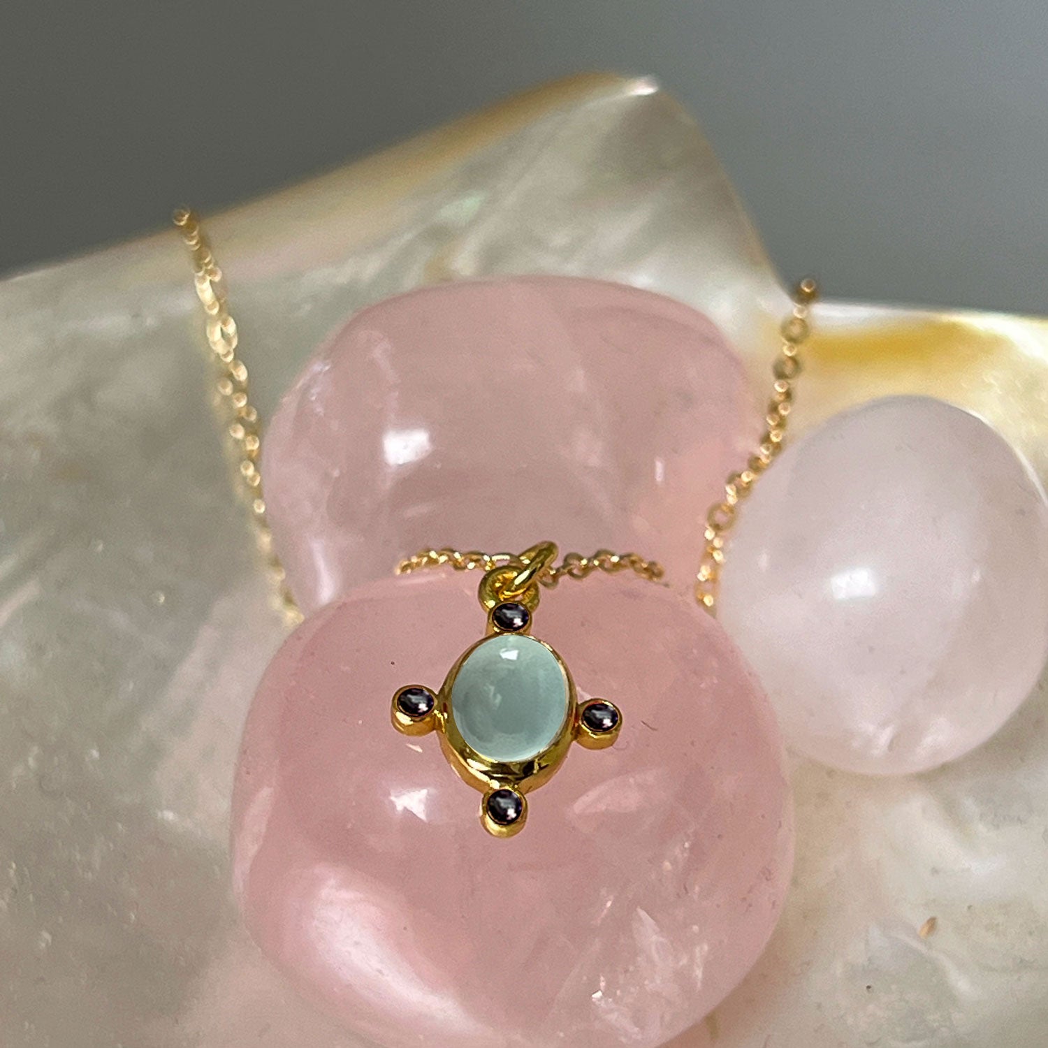 Aqua Chalcedony & Sapphire Zircon Pendant on a gold plated chain on a bed of pink crystals