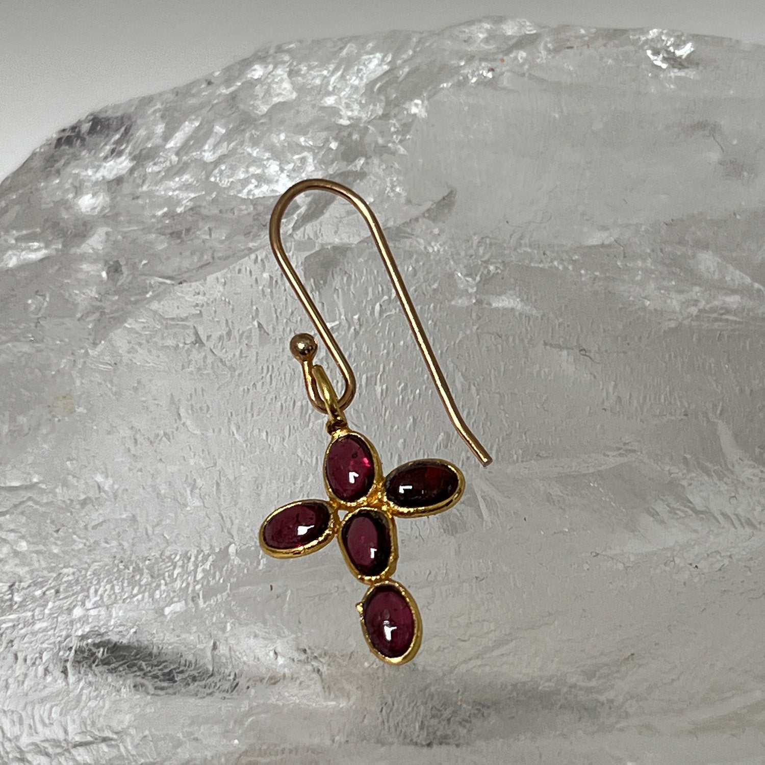 Gold cross earring with garnet gemstones on a crystal background
