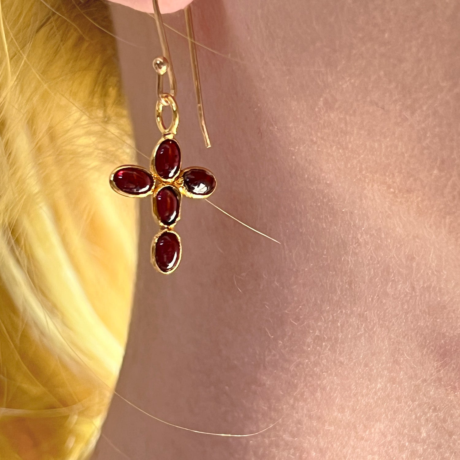 Gold earring with gold gemstones worn by a person with blonde hair.